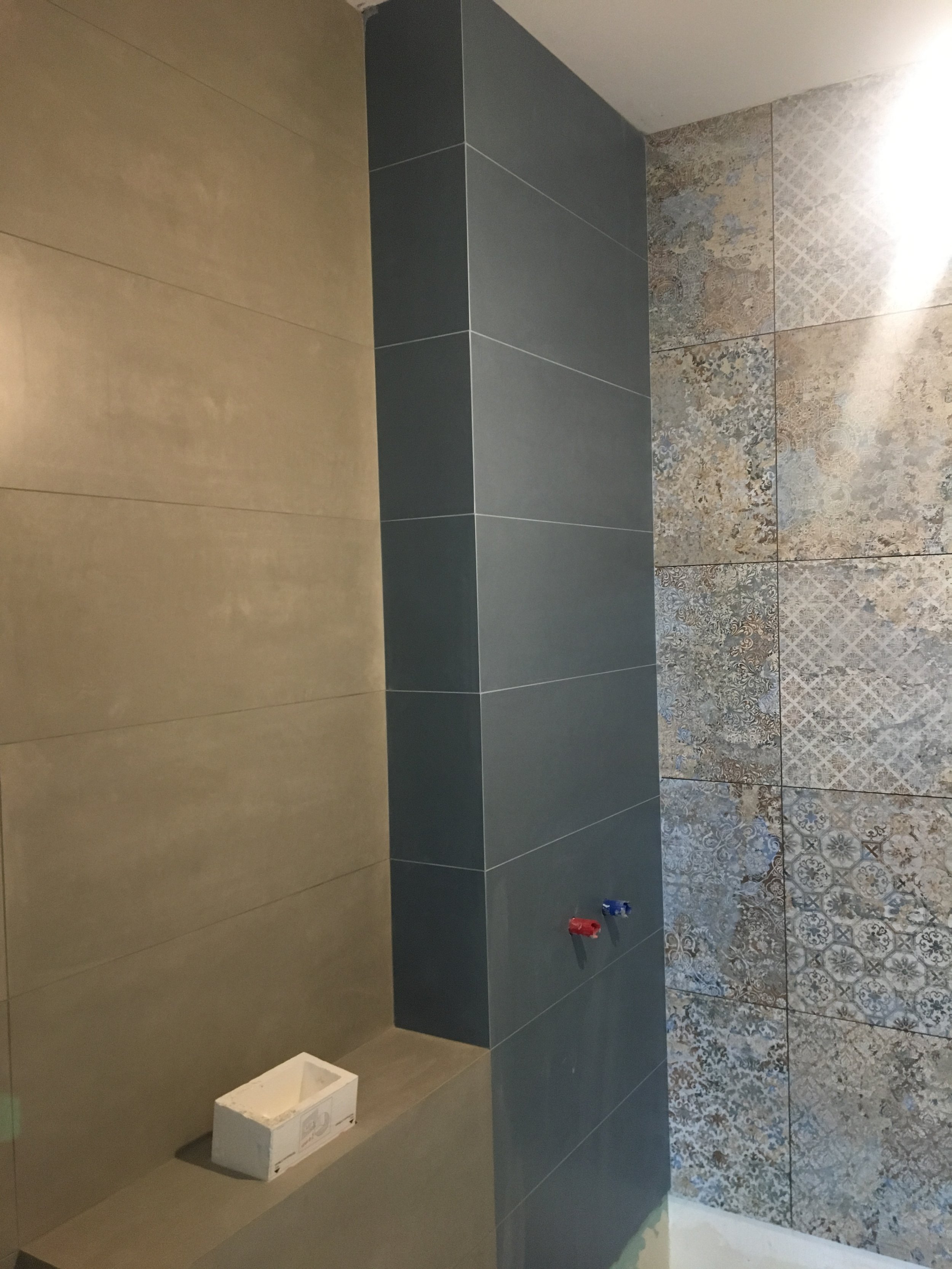 Close-up of a man with dark curly hair, wearing clear glasses, a nose ring, and a dark green sweater, looking off to the side with a slight smile.