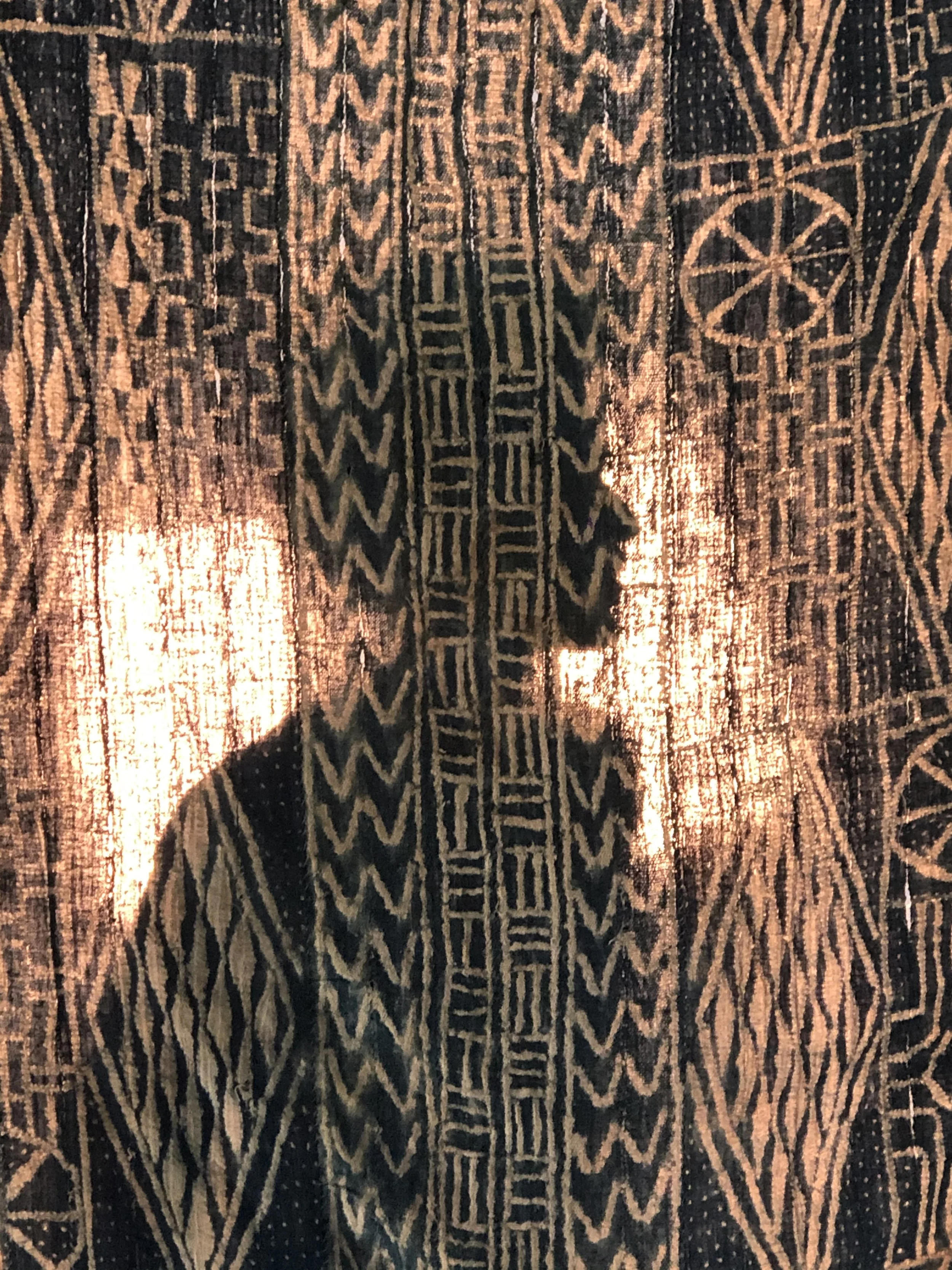 Silhouette d'un homme profilé, entourée de motifs géométriques africains sur un tissu décoratif camerounais ndop.