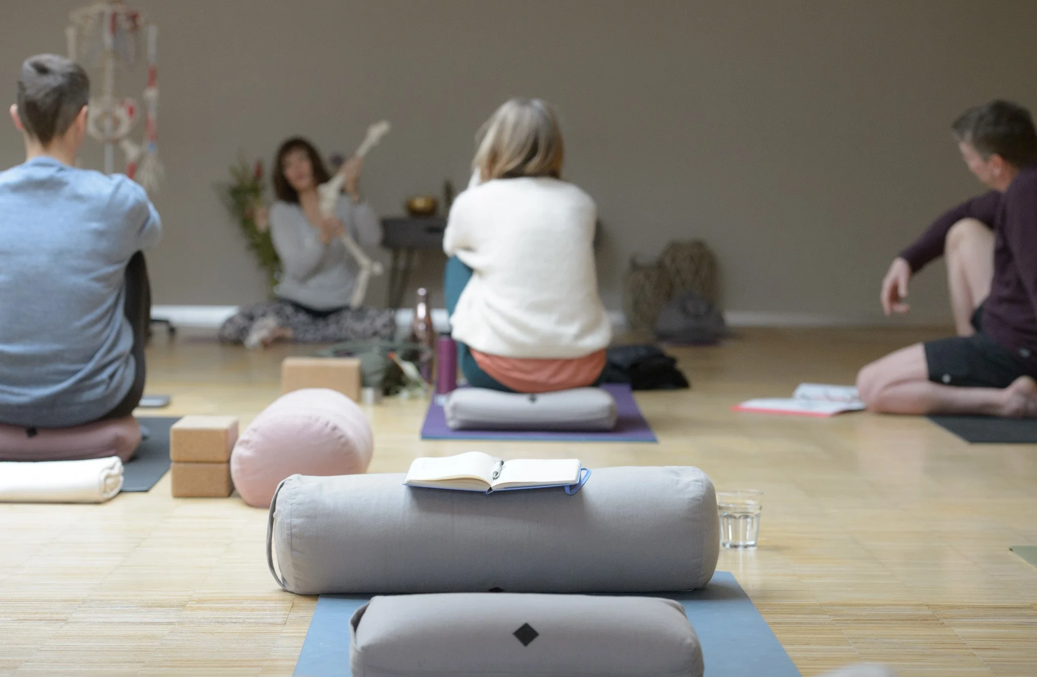 Menschen, die an einem Yogakurs oder einer Meditation im Raum teilnehmen, mit einer Frau in der vorderen Mitte, die eine Knochen-Inflationspuppe hält.