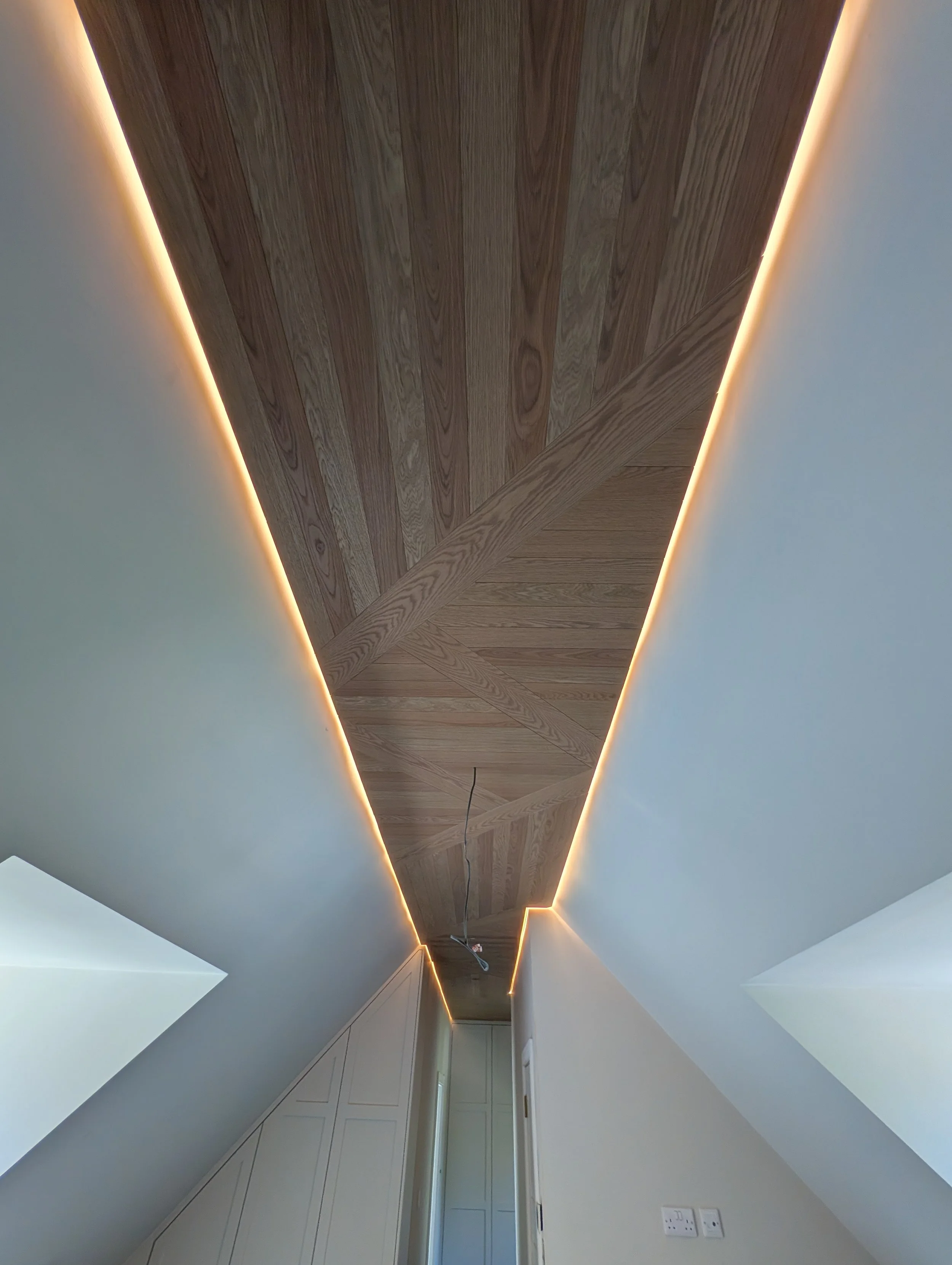 Bespoke geometric timber ceiling with integrated warm lighting by Clark & Prince