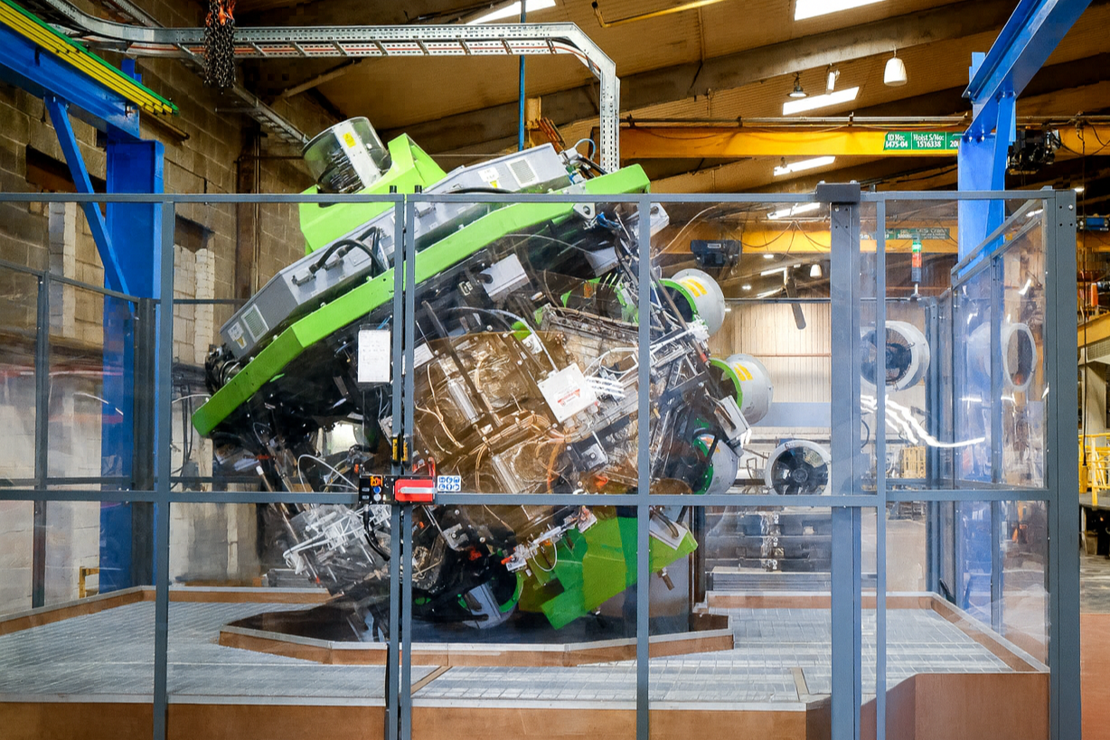 Large green and black machine enclosed in a clear protective casing inside an industrial warehouse. This is the Persico SMART Machine.