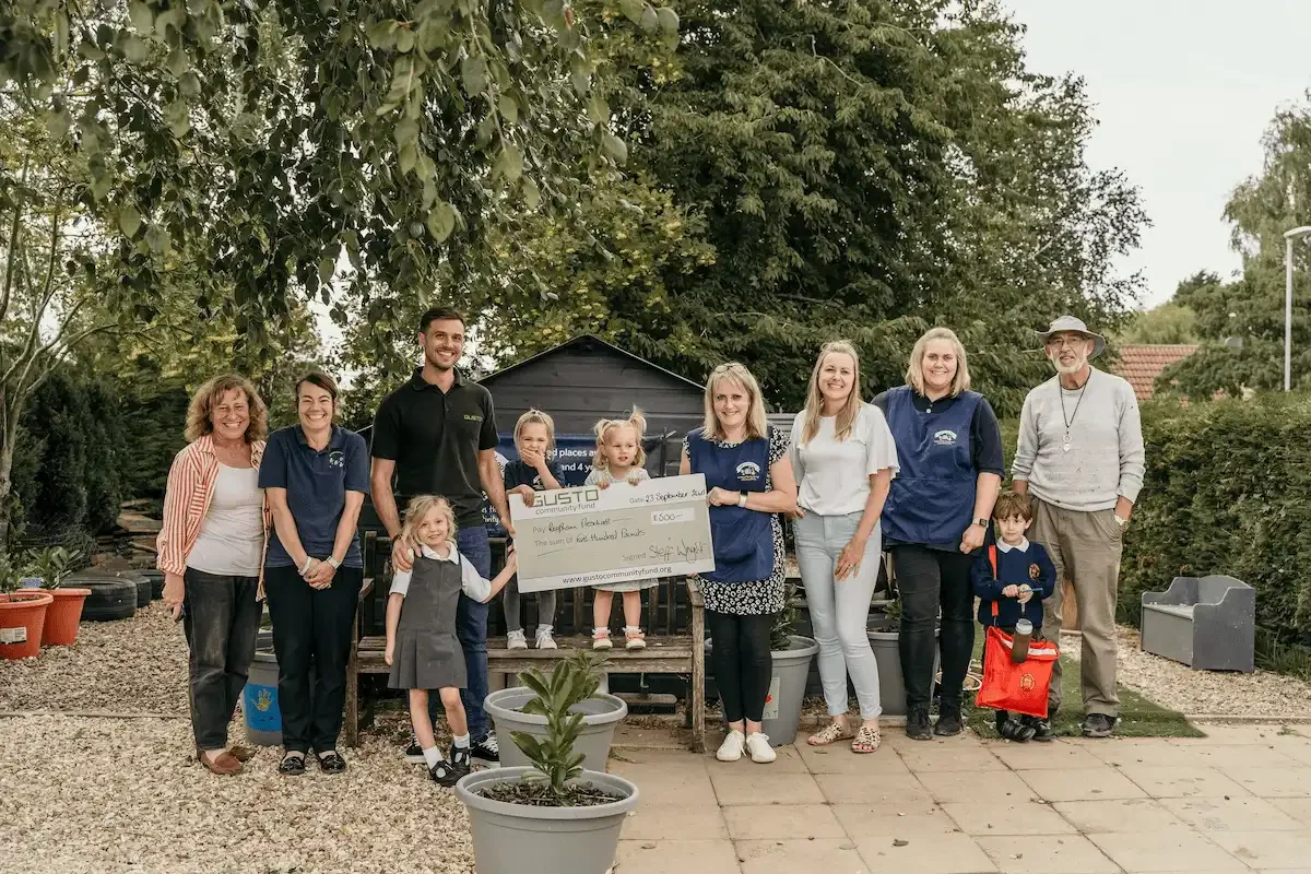 A Gusto employee stood with a number of staff members and children from Repham Preschool, holding a large cheque.
