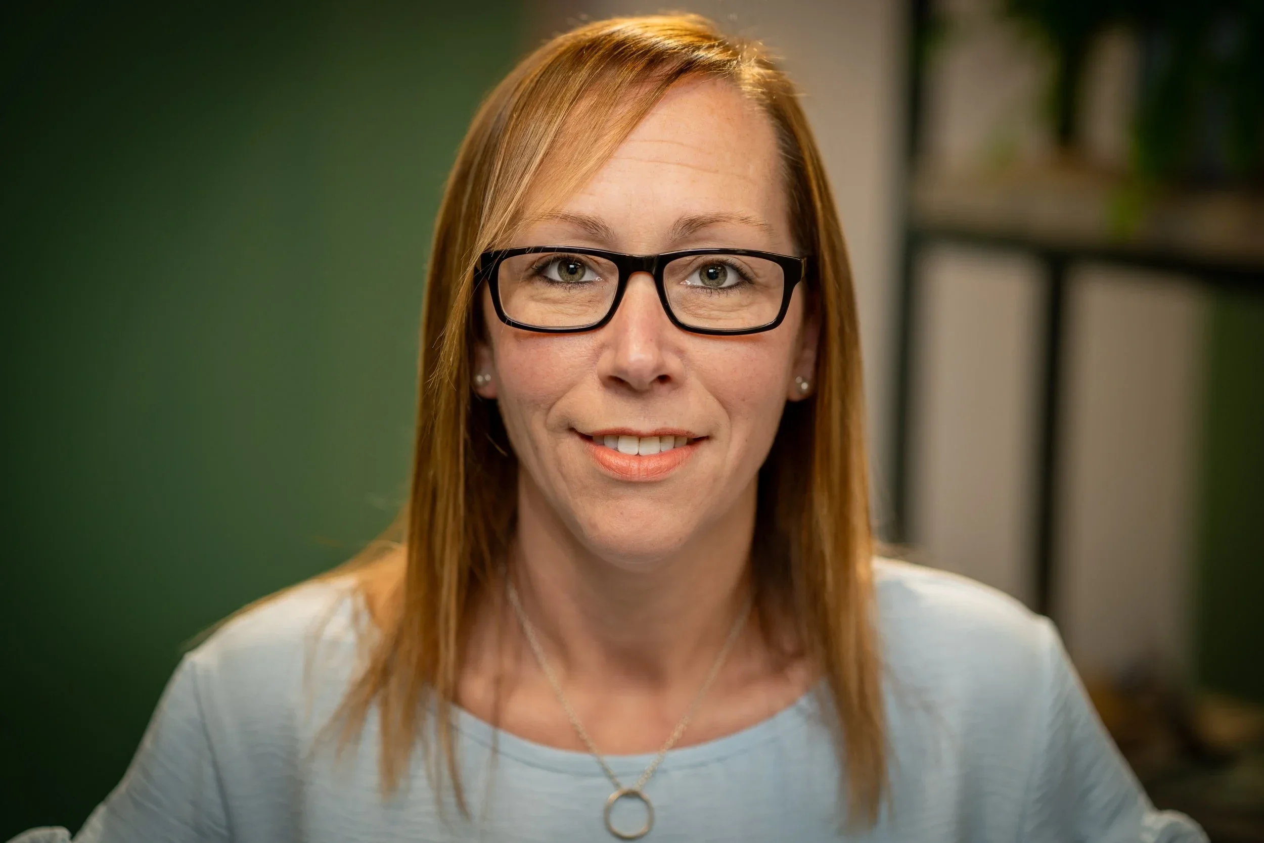 A headshot of a lady with blond straight hair and glasses staring at the camera and smiling