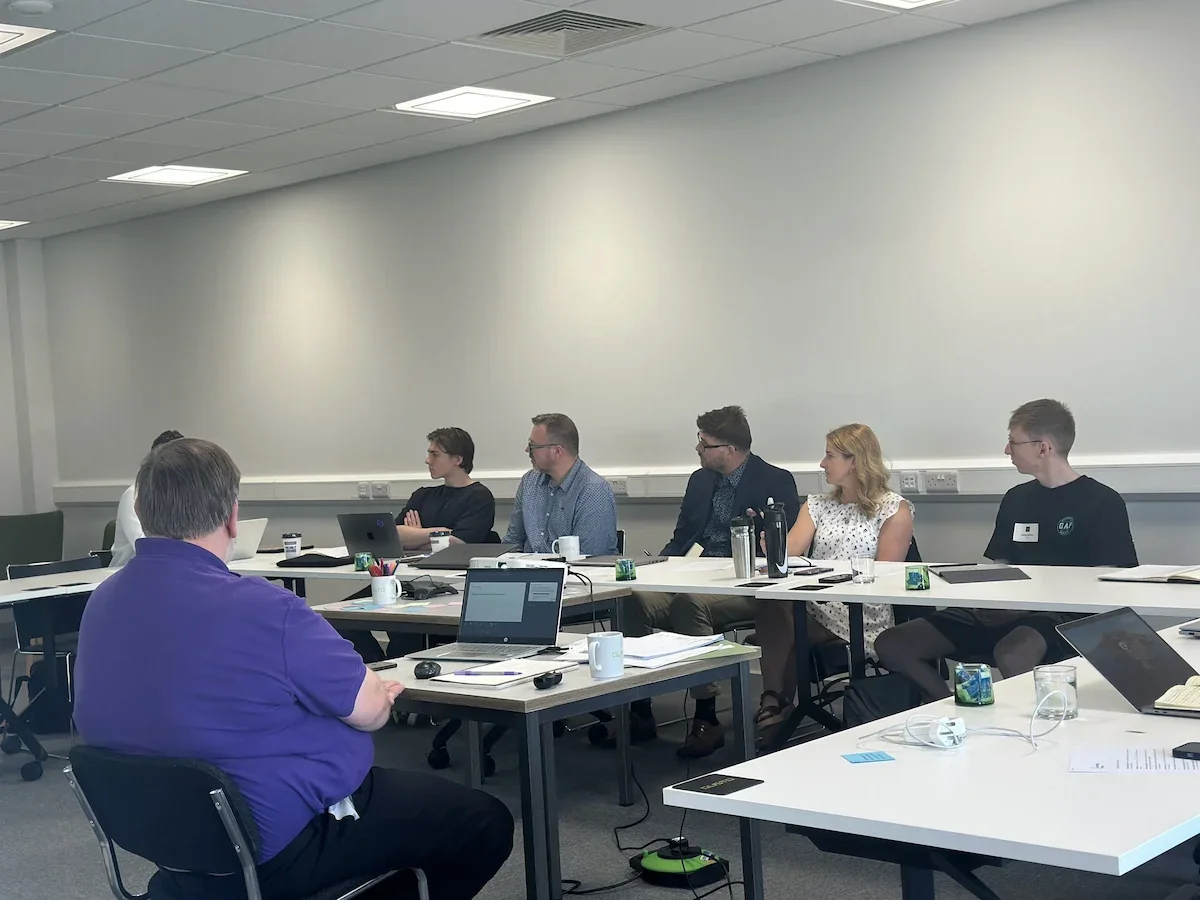 Several people sat in a u shaped laid out training roomwith laptops