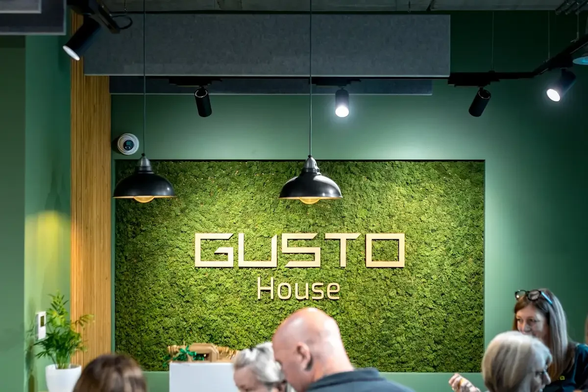 a number of people gathering at a reception area with a sign reading GUSTO House behind them