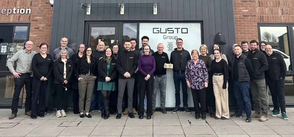 A large group of people stood in front of a modern office building smiling. The building is Gusto House.