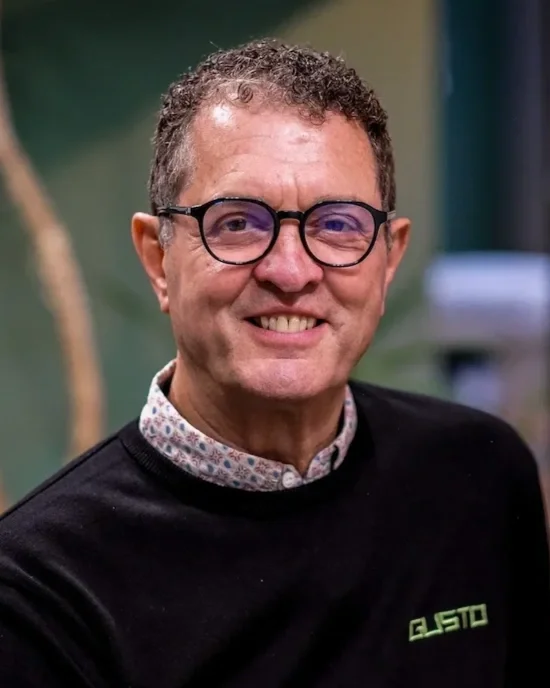 A middle-aged man with curly hair and glasses, wearing a checked shirt, standing indoors against a green and office background. Steff Wright