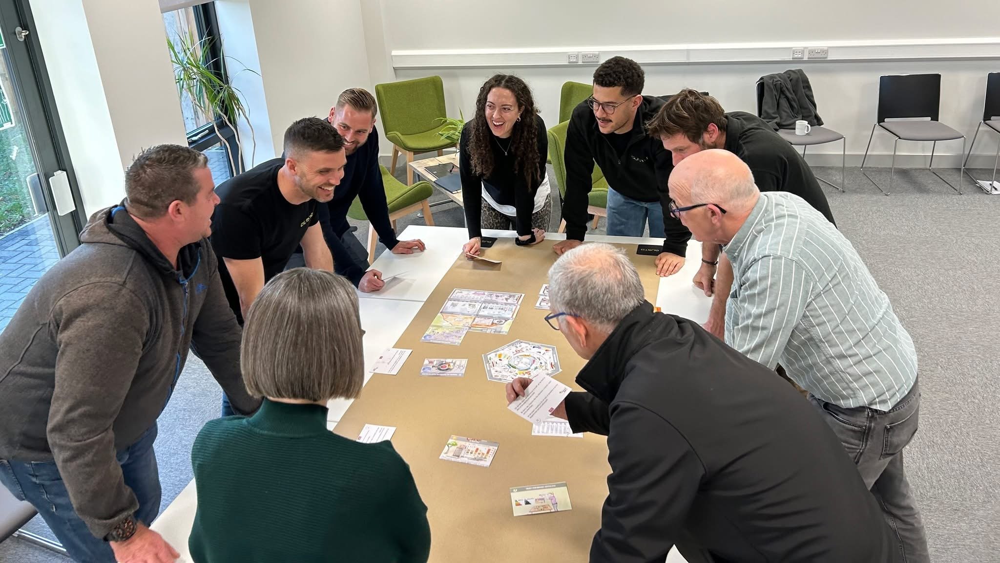 The Gusto Group team gathered around a table, leaning in to arrange cards and diagrams during a Climate Fresk sustainability training session.