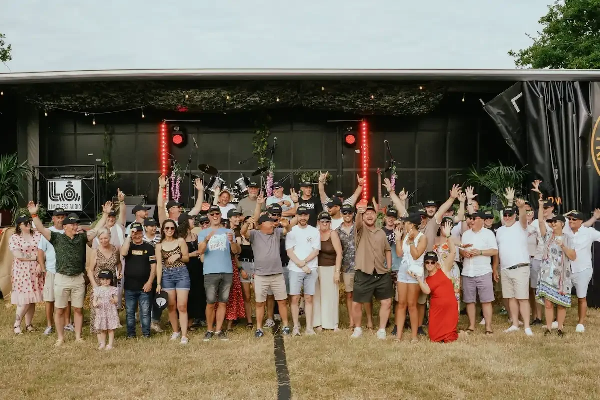 A large group of people stood in front of a stage. The people have their hands in the air cheering!