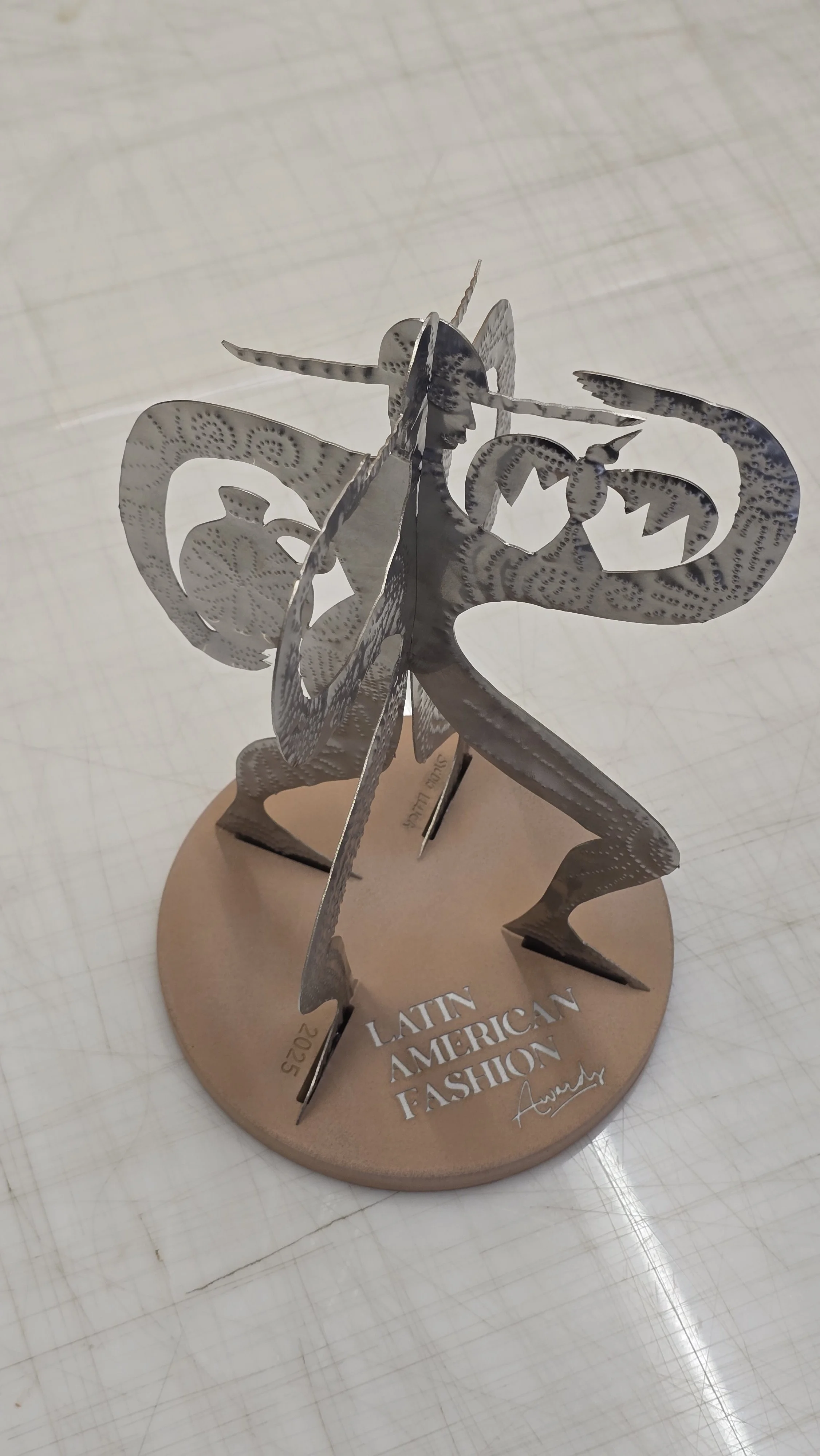 Award sculpture fabricated for the Latin American Fashion Awards, designed by José Campos, featuring a cut-out punched figure mounted on a mock stone terracotta base with debossed lettering.