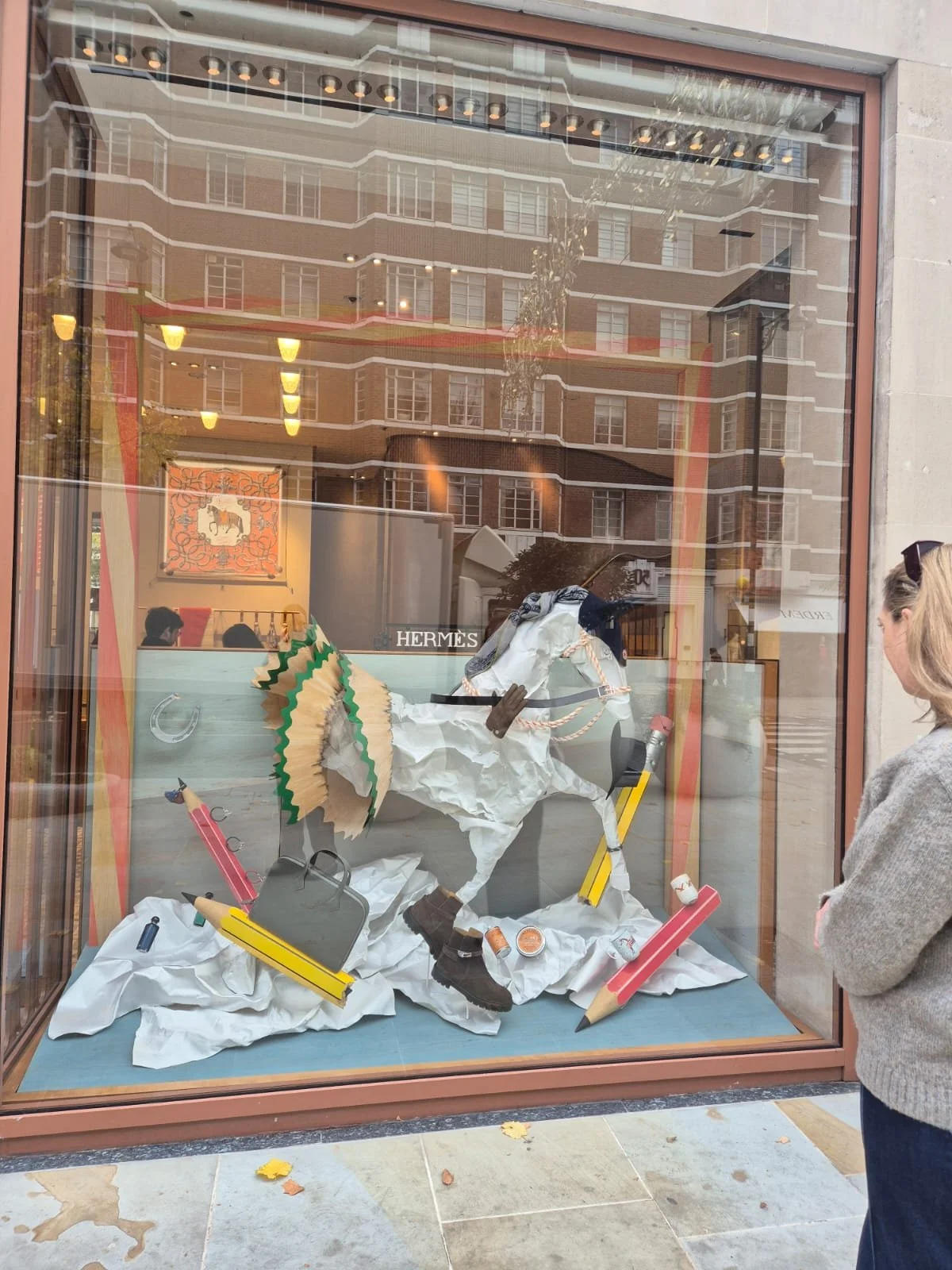 side angle view of the christmas window display for Hermès in London, designed by Shona Heath, featuring a sculptural horse emerging from a painted backdrop into a satin fabric snow landscape.
