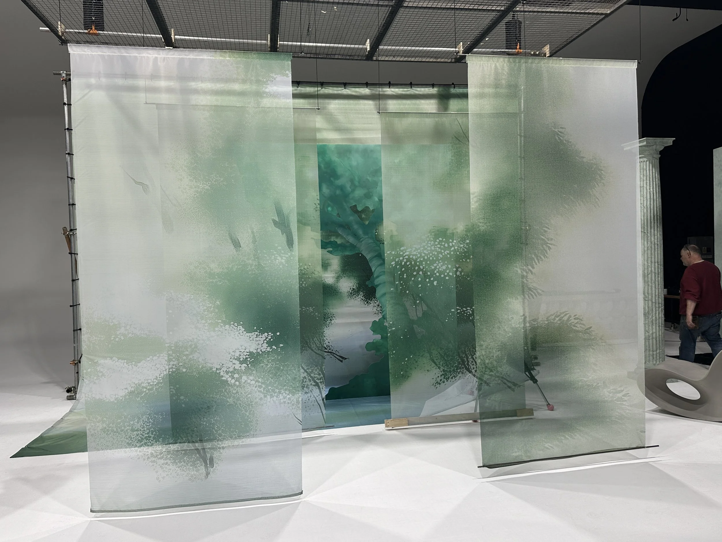 The completed scenic environment installed on location, combining multiple suspended translucent panels with a large-format scenic backdrop to achieve an immersive garden-inspired setting.
