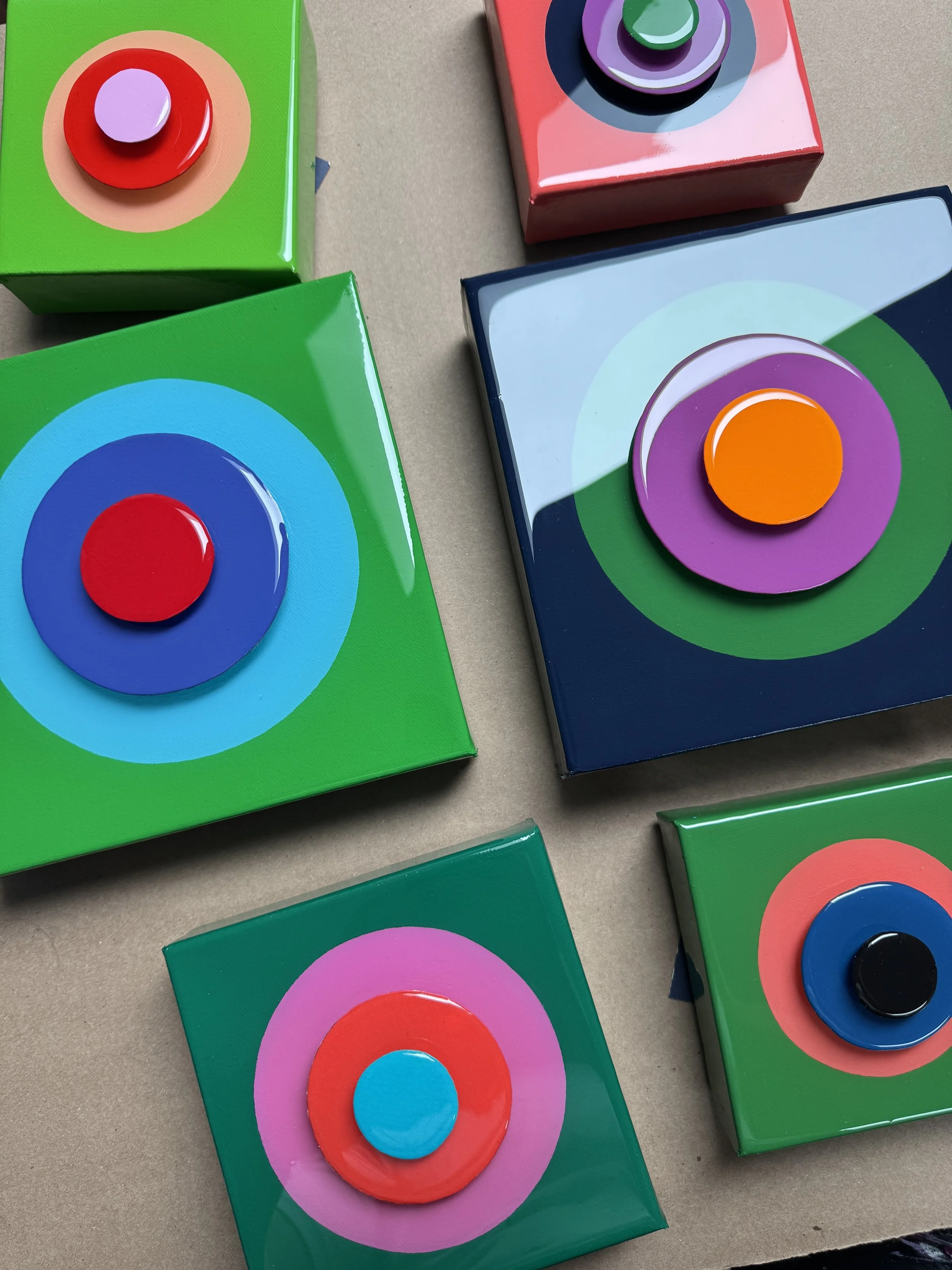 These small-scale Taking Aim pieces combine bold geometric compositions with layered dimensional elements and high-gloss resin surfaces. Exploring focus, direction, and personal momentum, each work uses vibrant color relationships and reflective fini