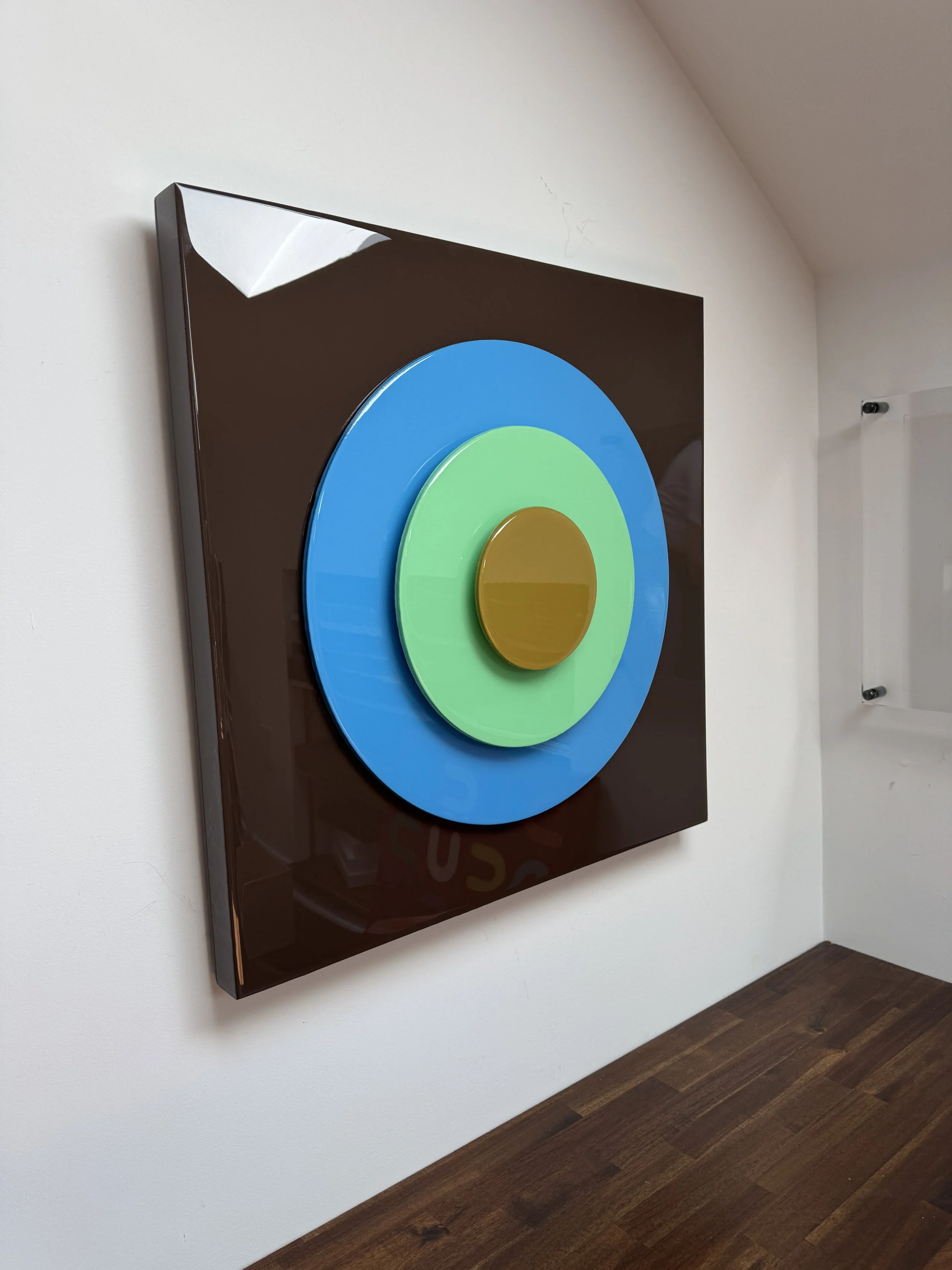 This custom Taking Aim installation for a Charlotte, NC home combines bold geometric simplicity with layered 3D construction and high-gloss resin finishes. The dimensional bullseye composition creates shifting reflections, depth, and shadow throughou