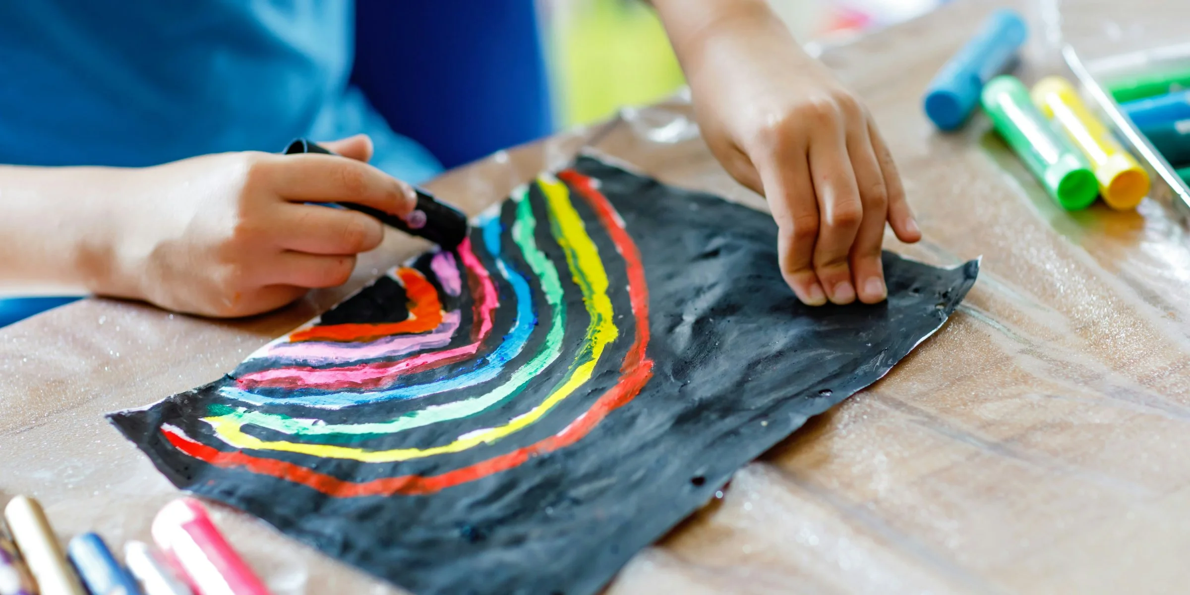 Close up photo of child drawing a rainbow with art supplies