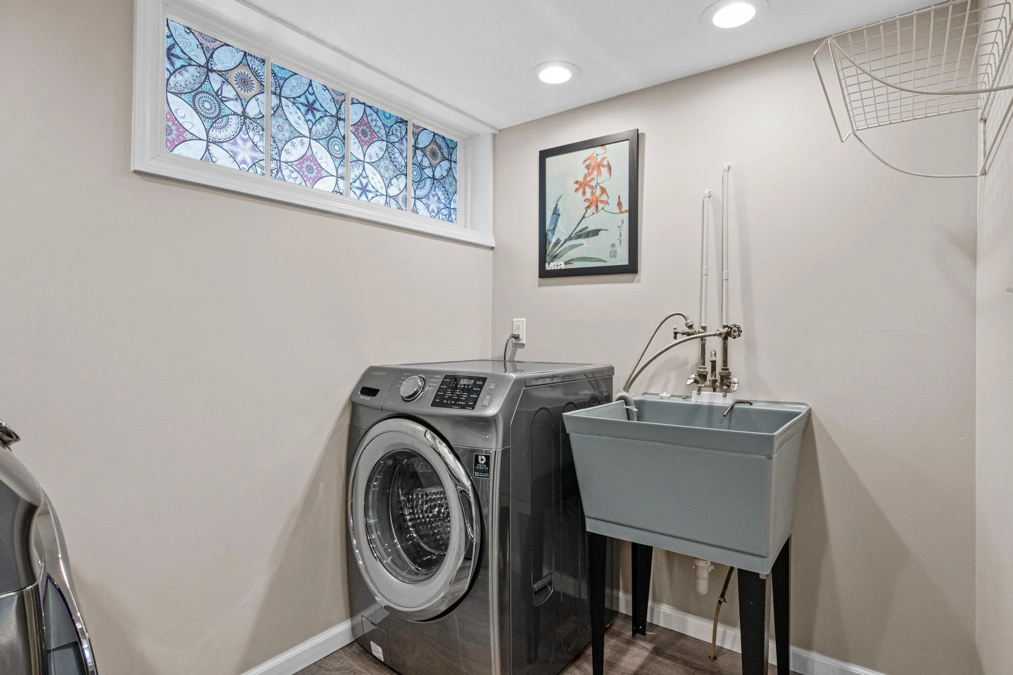 Laundry room with a silver washing machine, a gray utility sink, and a decorative window with blue and purple stained glass.