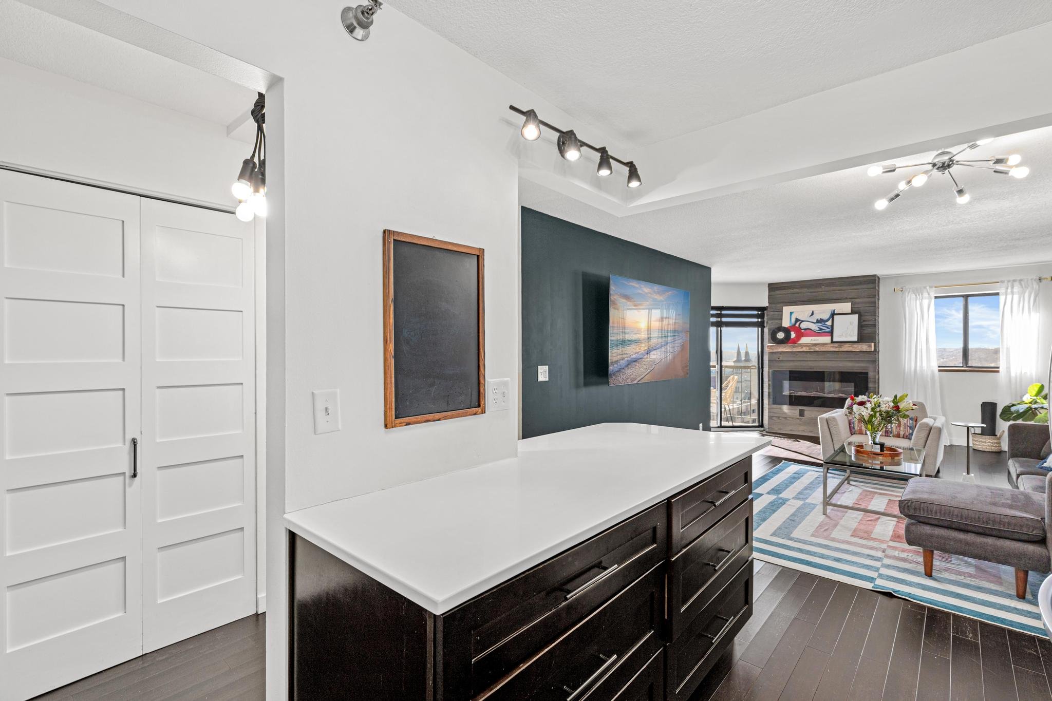 Living room with a dark wood dresser, white countertop, and a wall-mounted flat-screen TV showing a beach sunset.