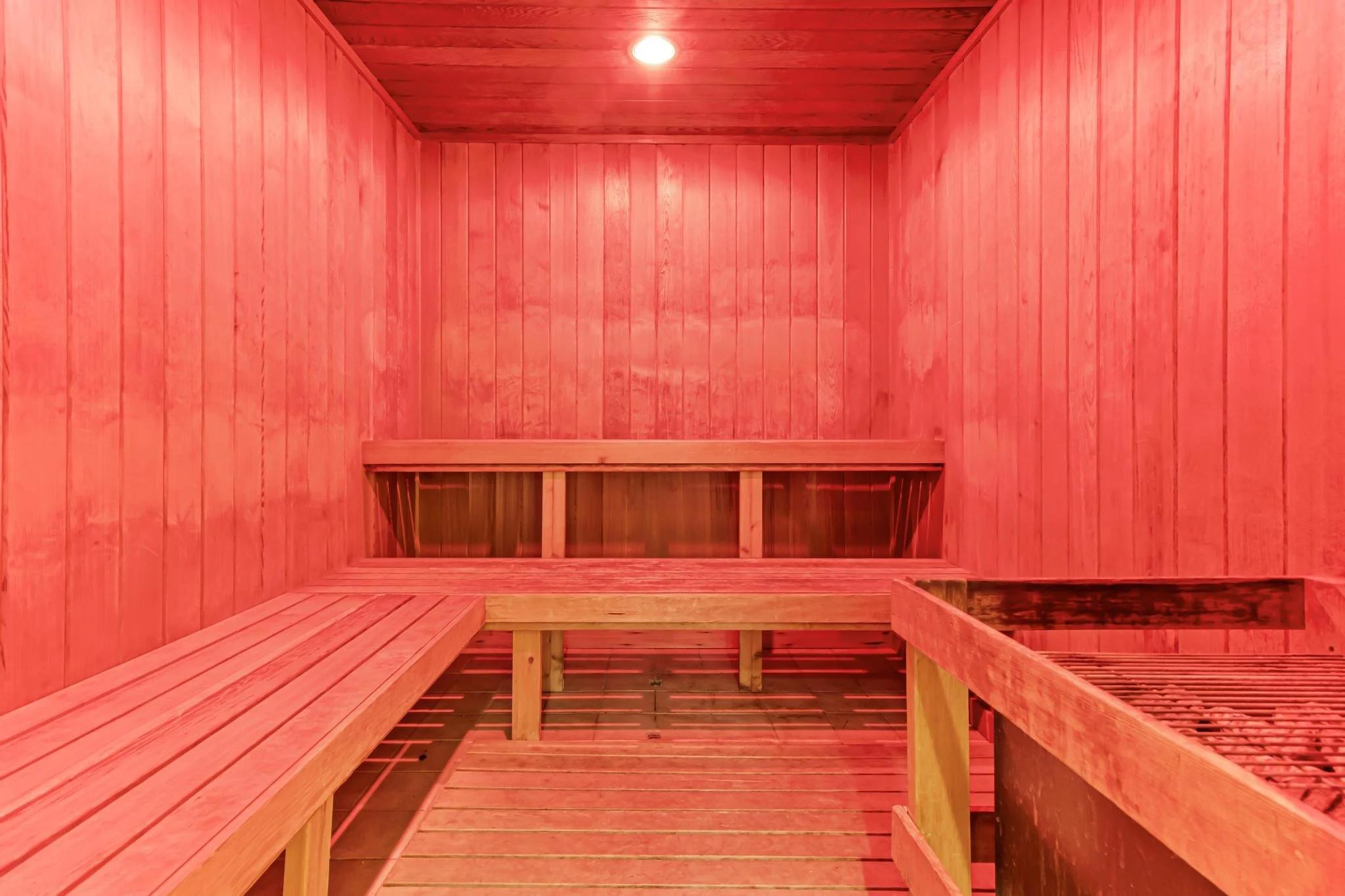 Interior view of a traditional Finnish sauna with wooden benches and walls, illuminated by a ceiling light.