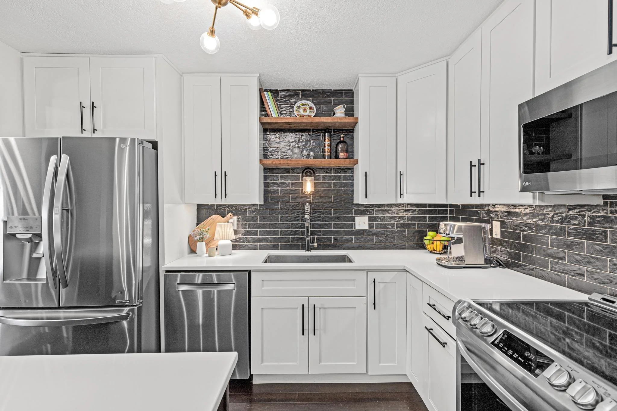 Modern kitchen with white cabinets, black subway tile backsplash, stainless steel appliances, open shelves with decorative items, and a black countertop.