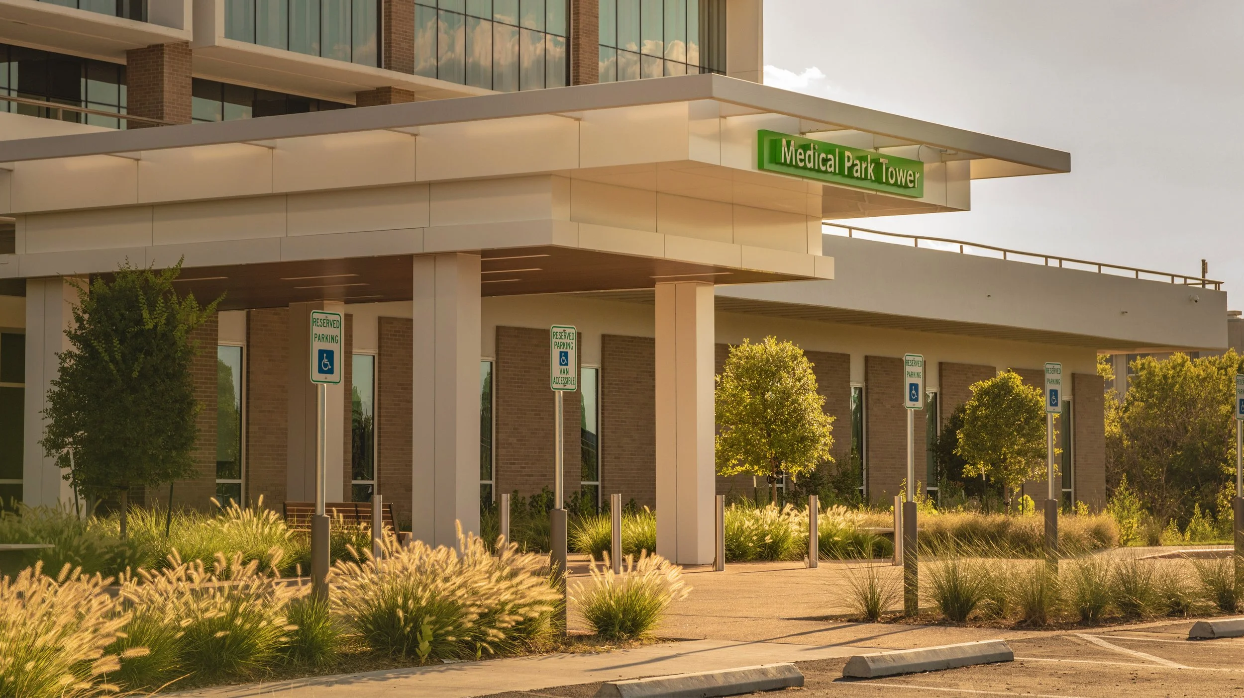 Exterior view of Medical Park Tower with reserved parking for handicapped spaces, greenery, and a modern building facade.