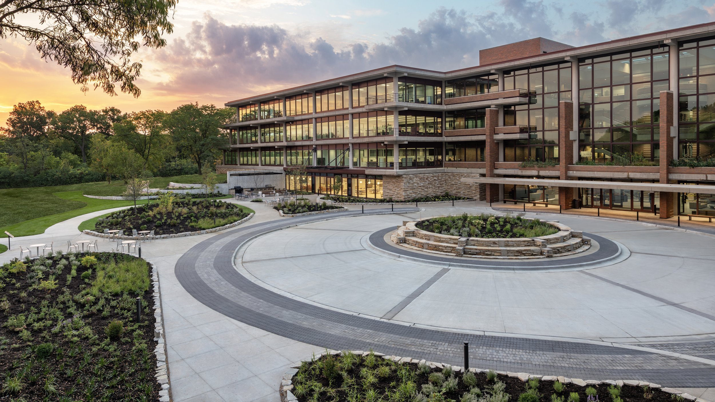 Modern multi-story office building at sunset with landscaped courtyard and walking paths