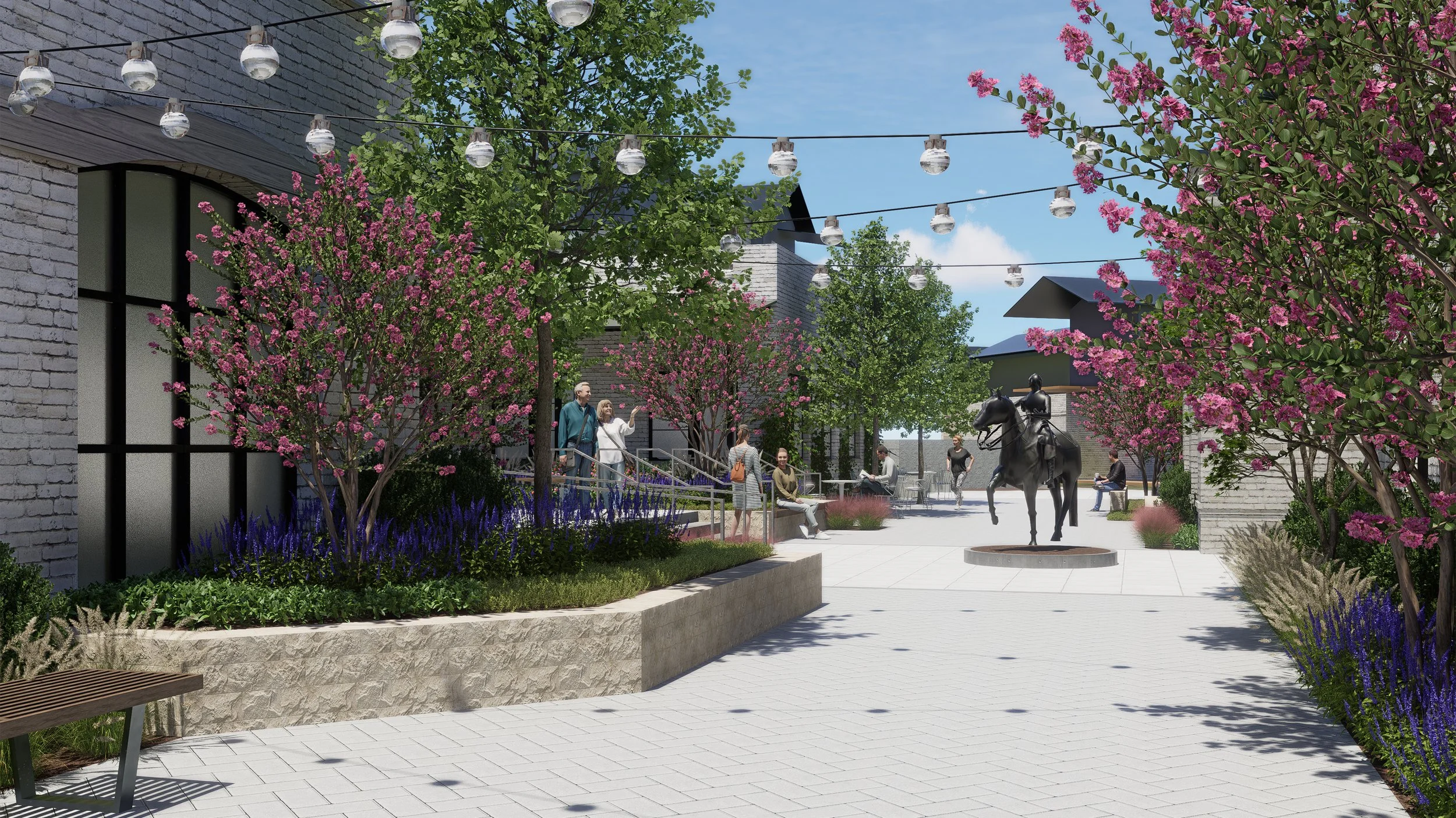 A plaza with trees and pink blossoms, a statue of a horse and rider, and people sitting and walking on paved paths under string lights and a blue sky.