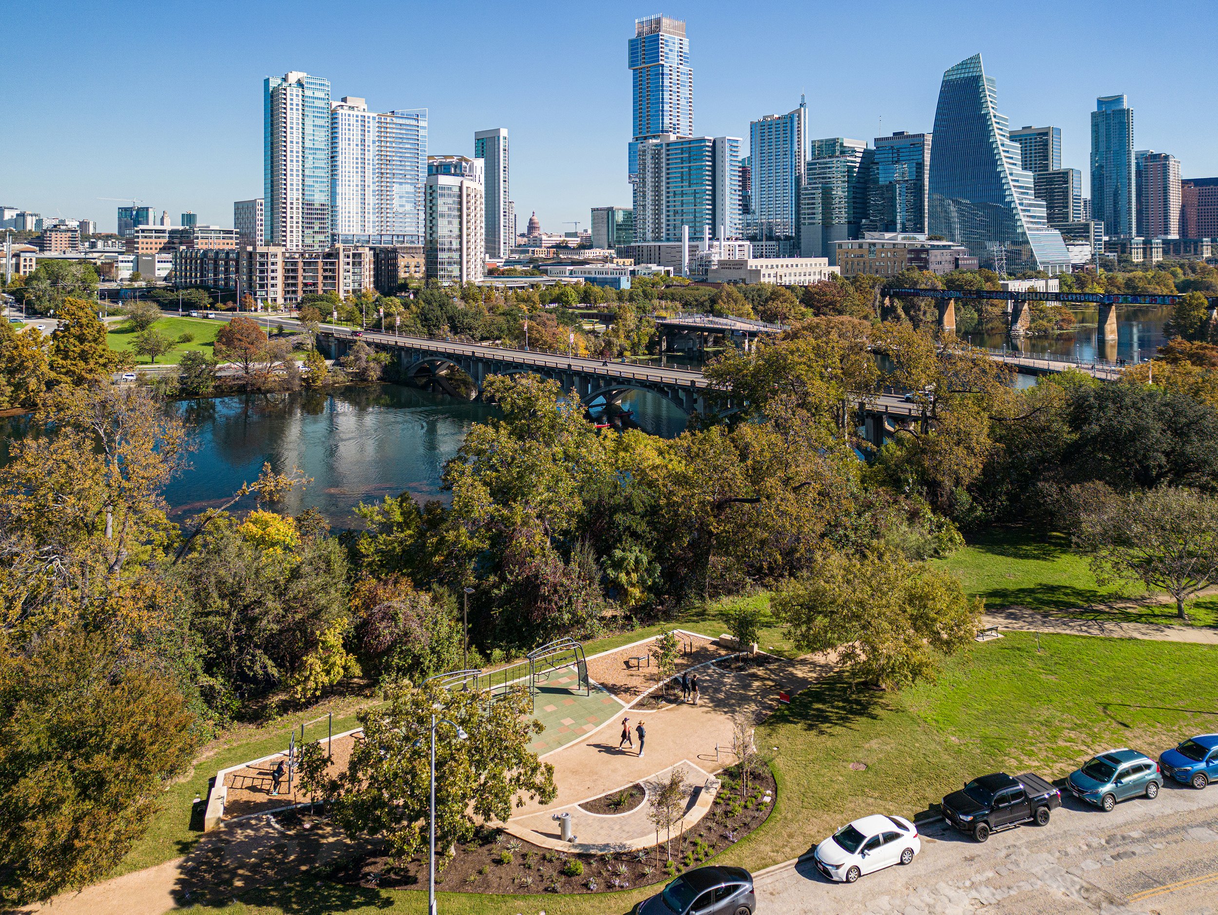 View of downtown Austin Texas skyline with tall skyscrapers, green park, and river in the foreground on a clear day.