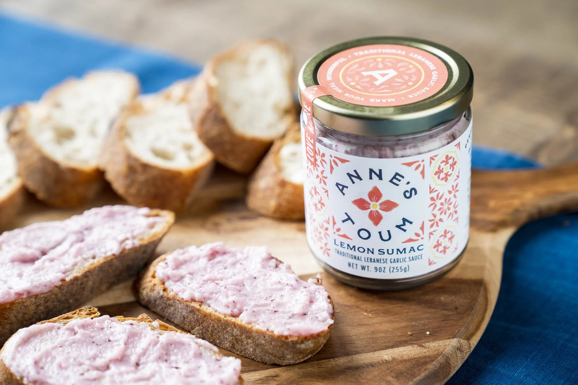 Jar of Annie's Toun Lemon Sumac on wooden tray with sliced bread topped with pinkish spread.