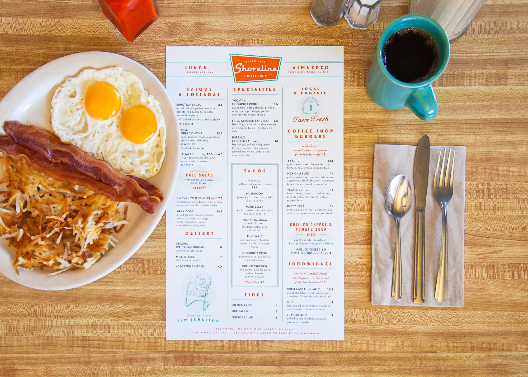 Shoreline Coffee Shop menu on a wooden surface next to a plate of food, a cup of coffee and silverware