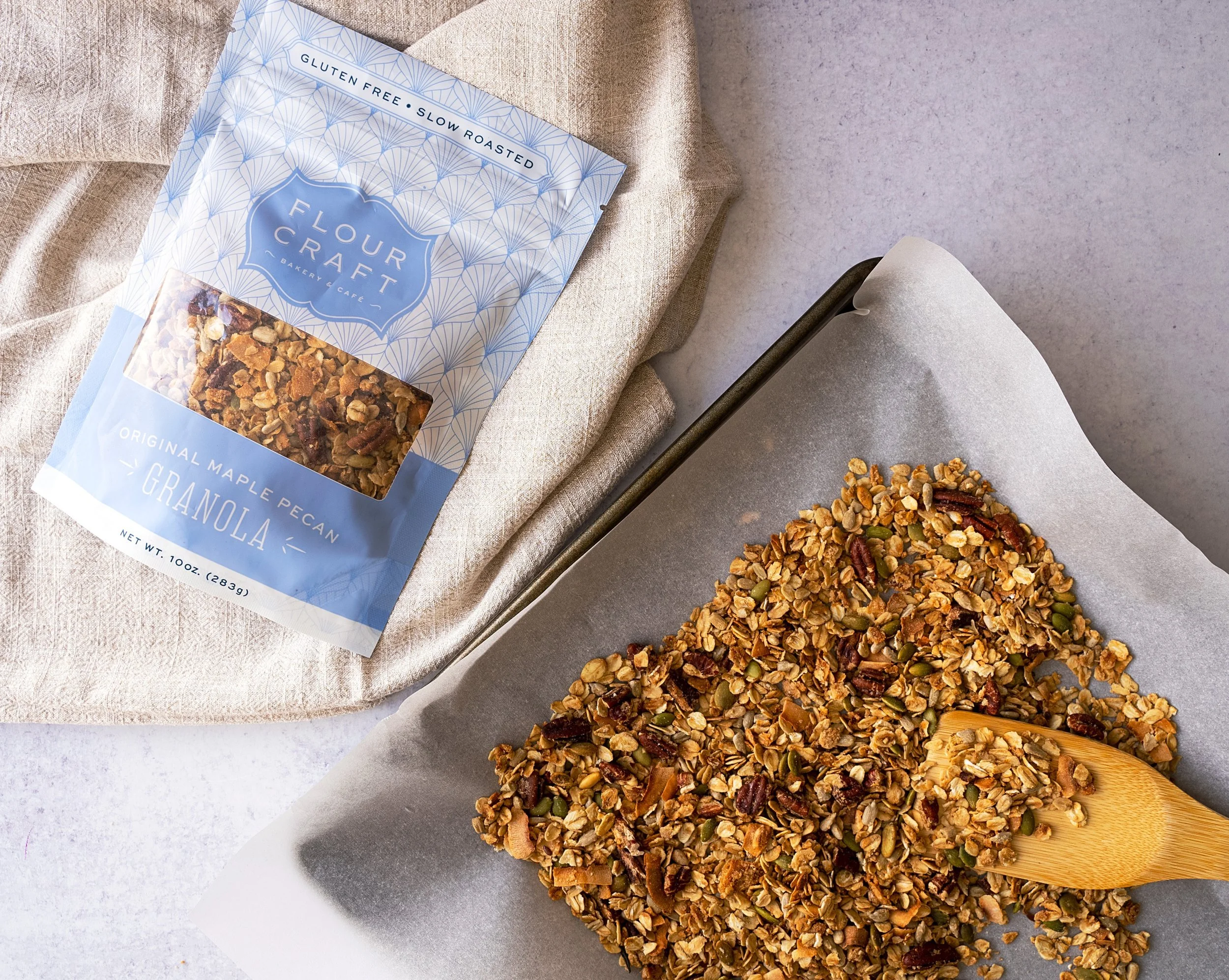 A tray of granola with pumpkin seeds, pecans, and other grains, next to a package of Maple Pecan Granola from Flour Craft Bakery and Cafe.