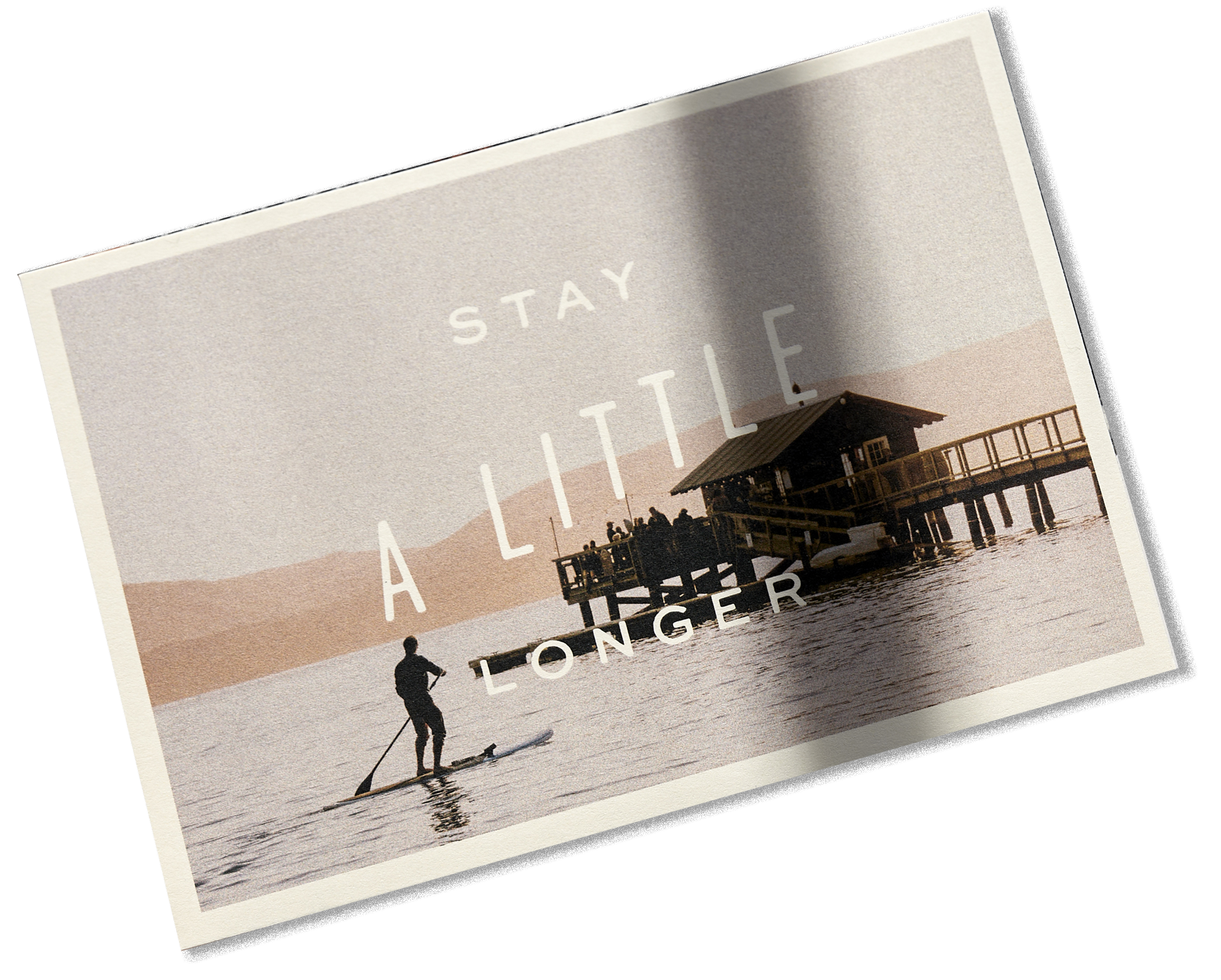 A sunset scene at a pier with a person paddleboarding on calm water and a small wooden structure with a group of people on the deck, overlaid with the text "Stay A Little Longer."