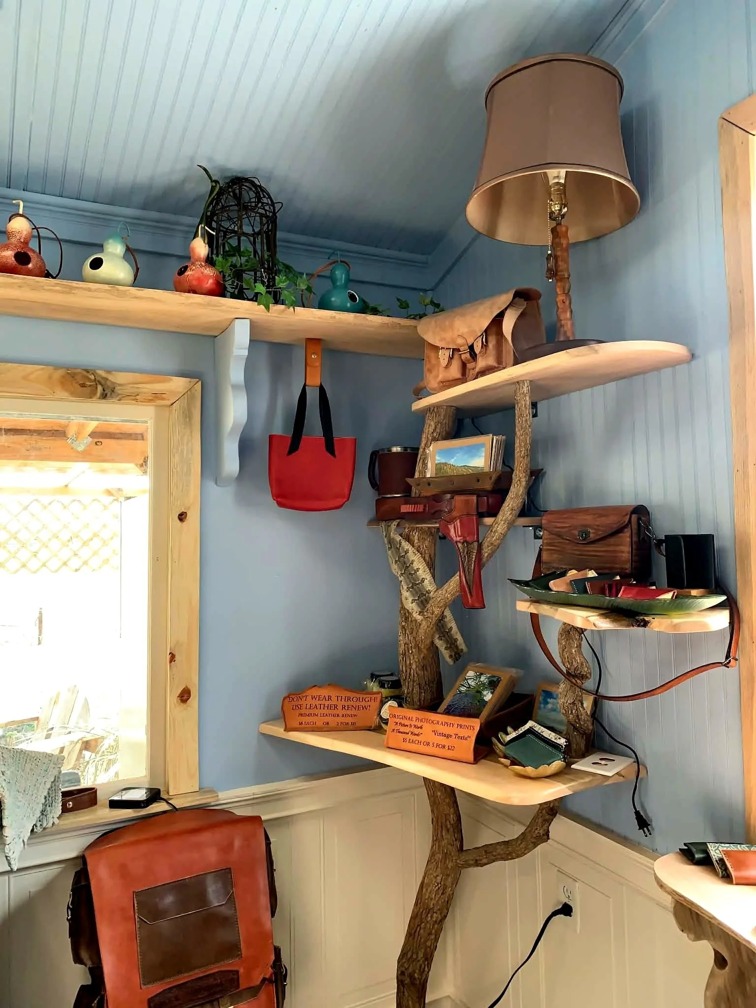 Beautiful handstiched leather goods hanging and sitting on hand made wood shelfs with branches.