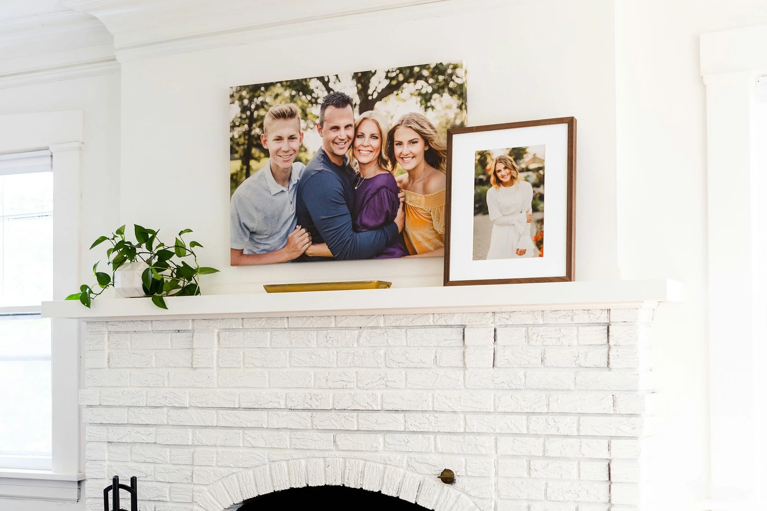 White brick fireplace with framed family photos on mantel, a potted plant on the left, and a brass object on the right