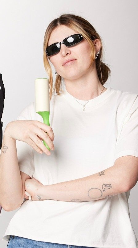 Maryn Worhacz wearing sunglasses holding a lint roller in front of a plain background.