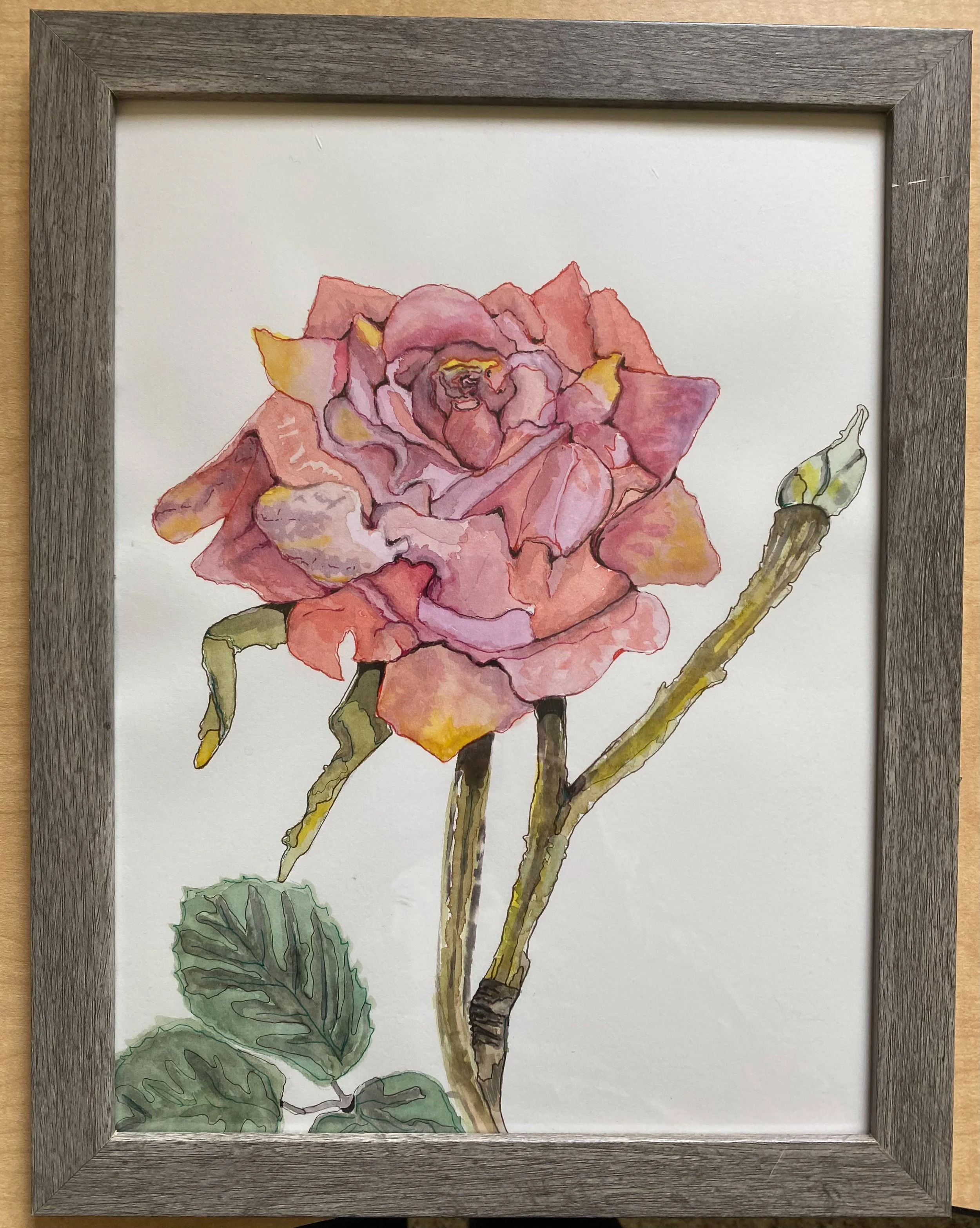 A watercolor painting of a pink rose with green leaves and a bud, framed in a wooden frame.