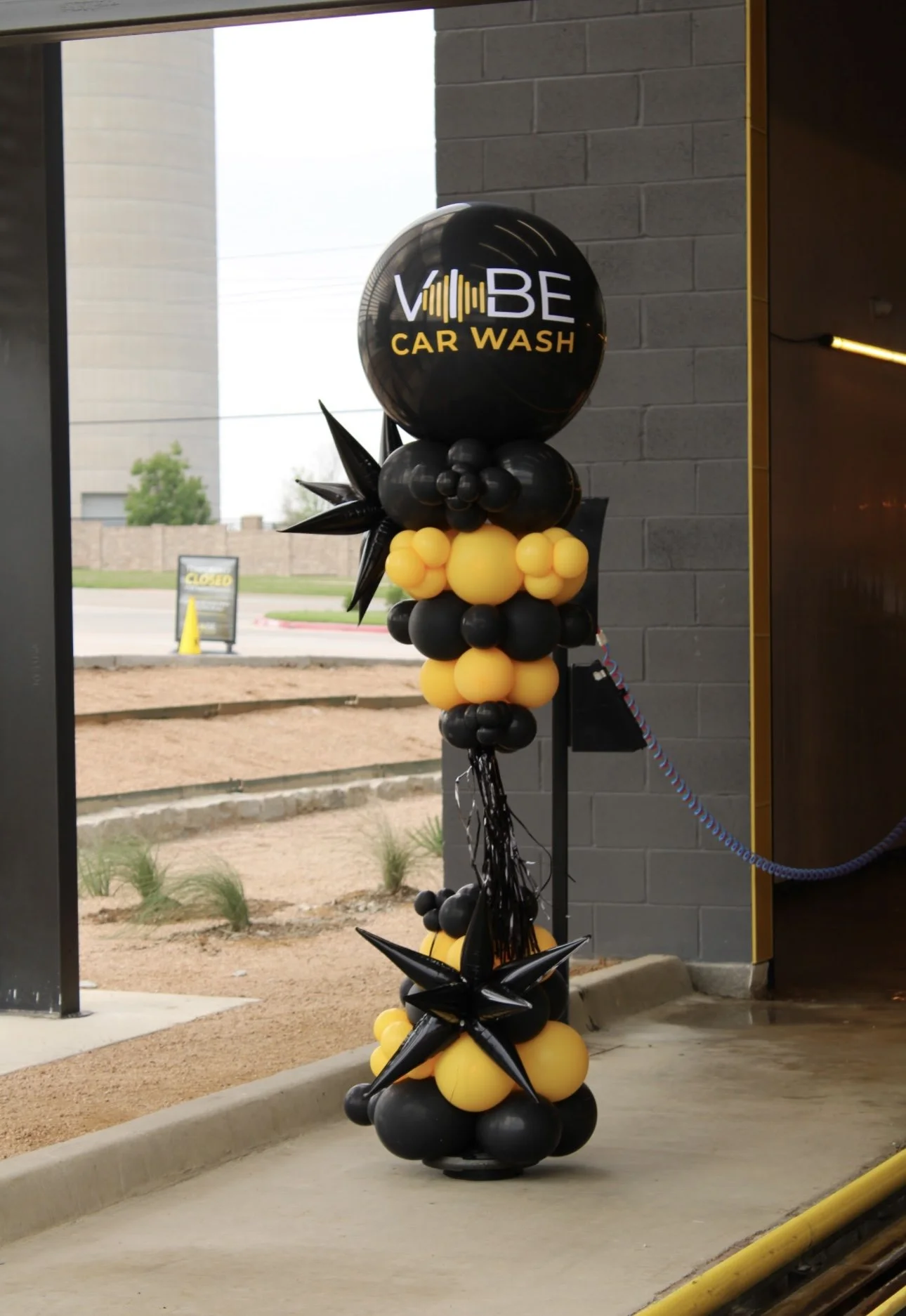 Decorative balloon arrangement outside a car wash with a black and yellow theme and a sign reading 'VIBE CAR WASH' at the top.