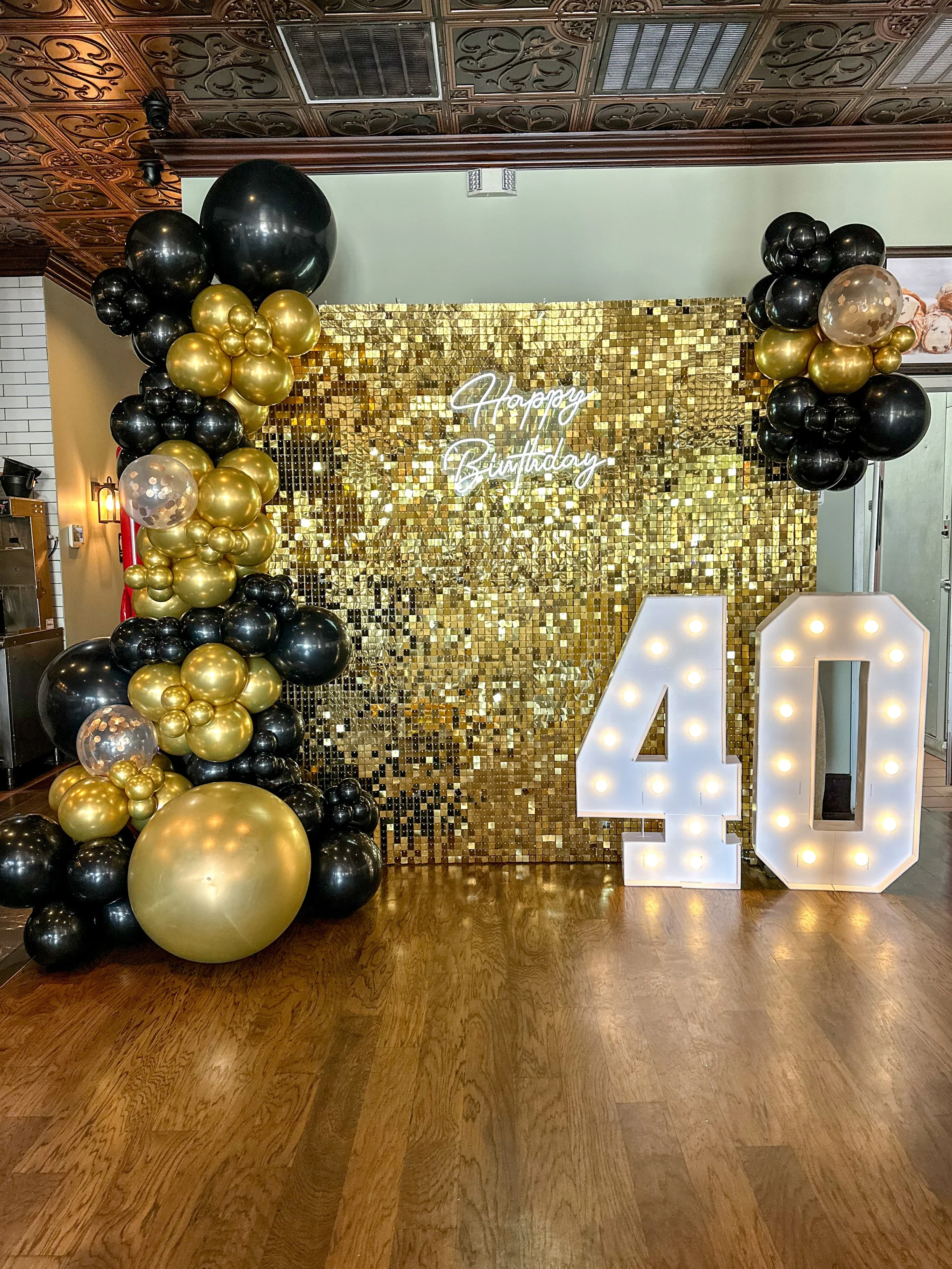 Gold and black balloon arch, illuminated "40" sign, and a gold mosaic backdrop with a neon "Happy Birthday" sign