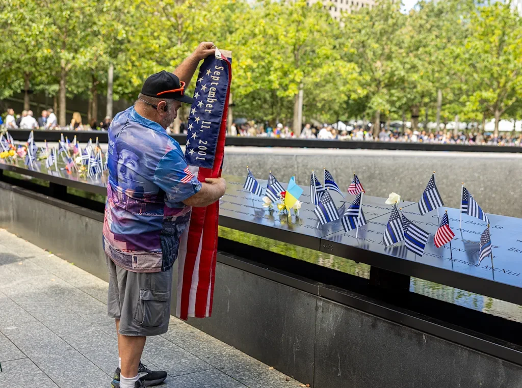 Visitor holding a September 11, 2001 flag at the 9/11 Memorial pool on the 25th anniversary