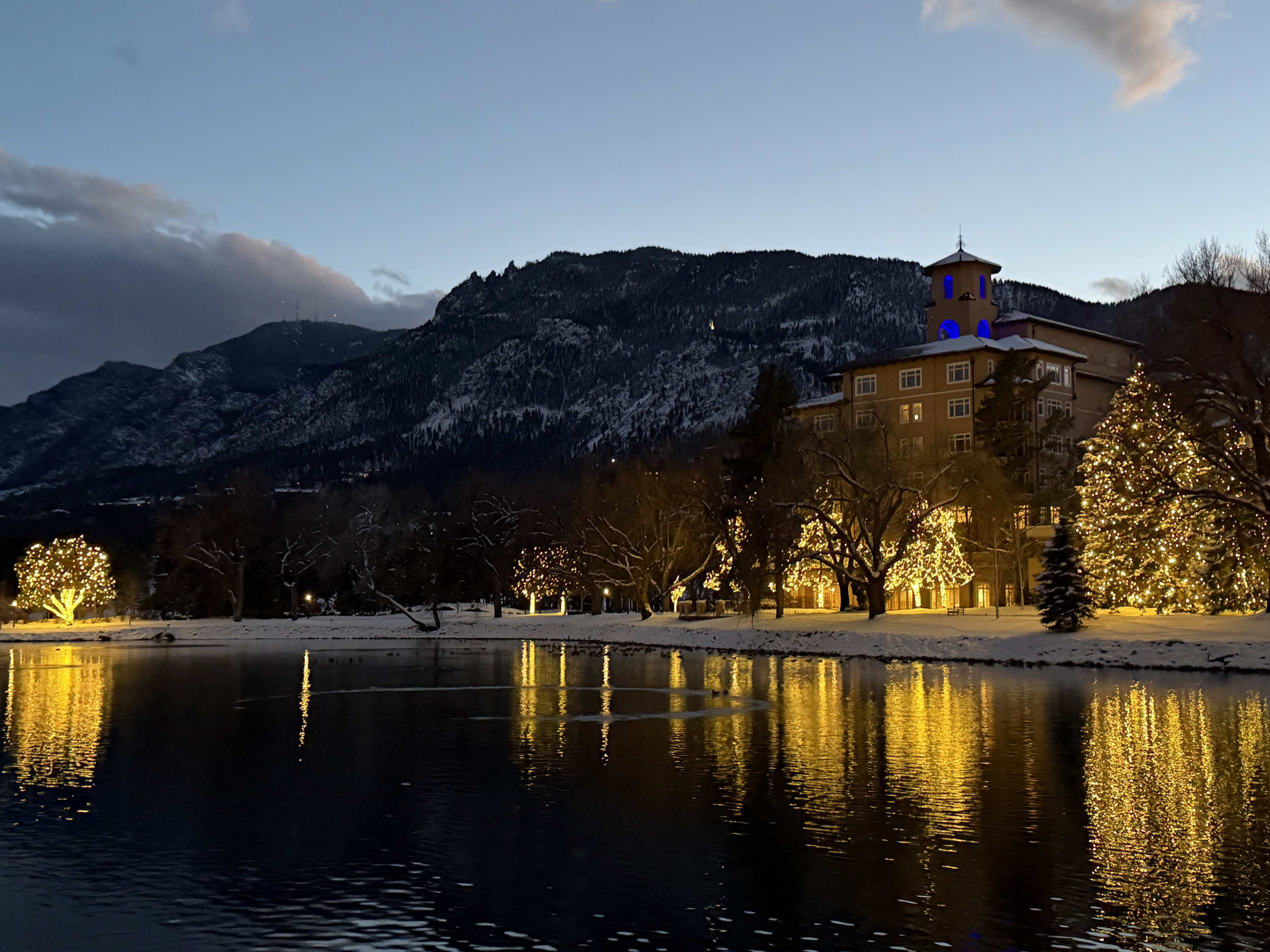 NatCon conference resort at dusk with holiday lights reflected in a lake below snowy mountains