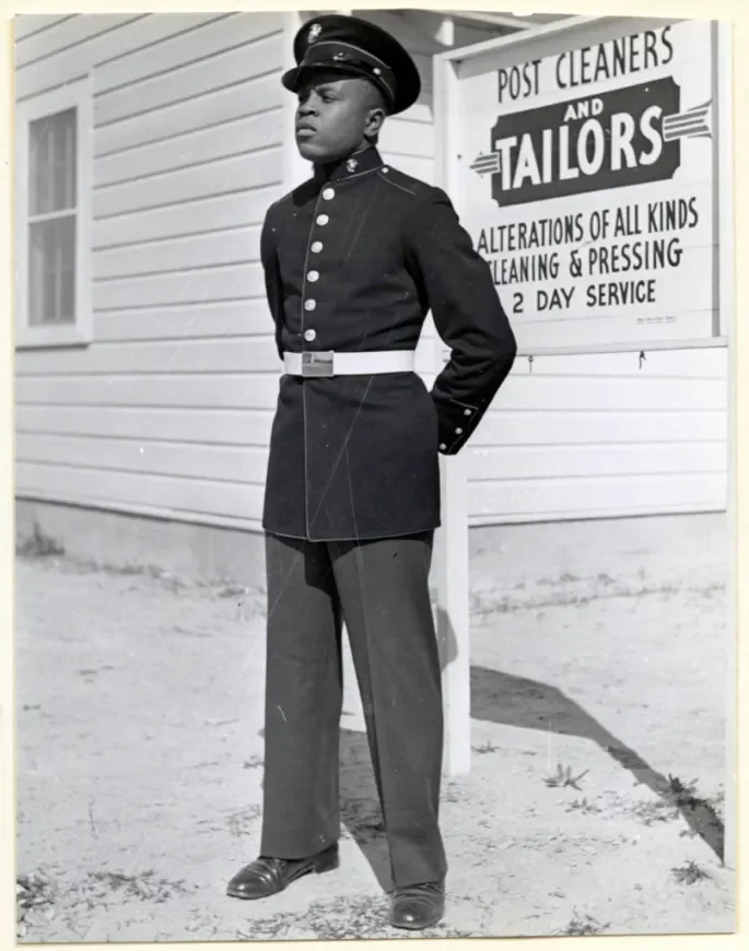 Historic black and white portrait of a Montford Point Marine standing in dress blues outside a base tailor shop
