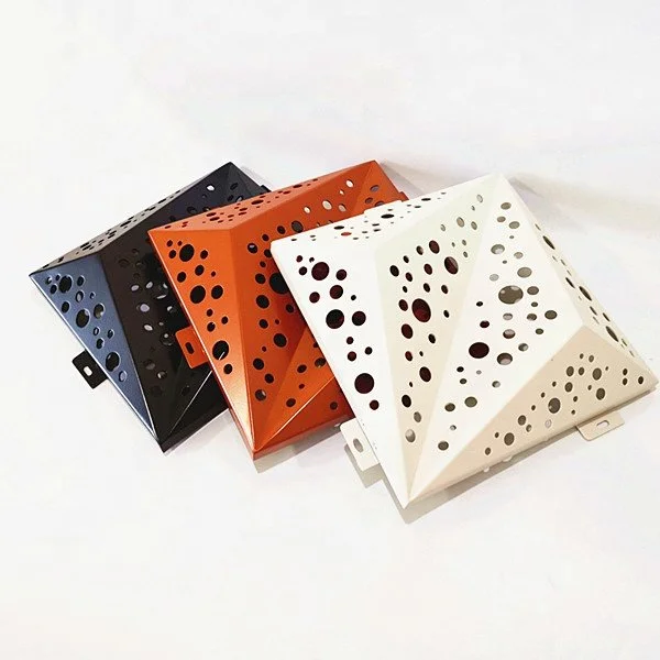 Three geometric, pyramid-shaped objects with multiple circular holes, colored black, orange, and white, placed on a white surface.