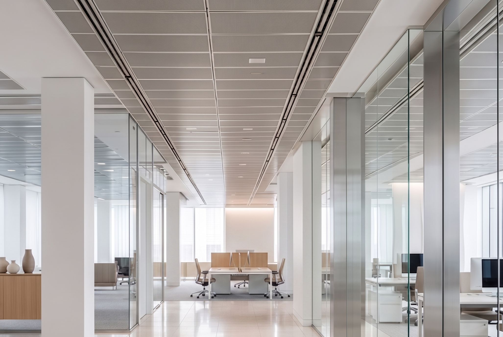 Modern corporate office lobby with glass walls, beige sofas, polished floors, and a high ceiling with integrated lighting.
