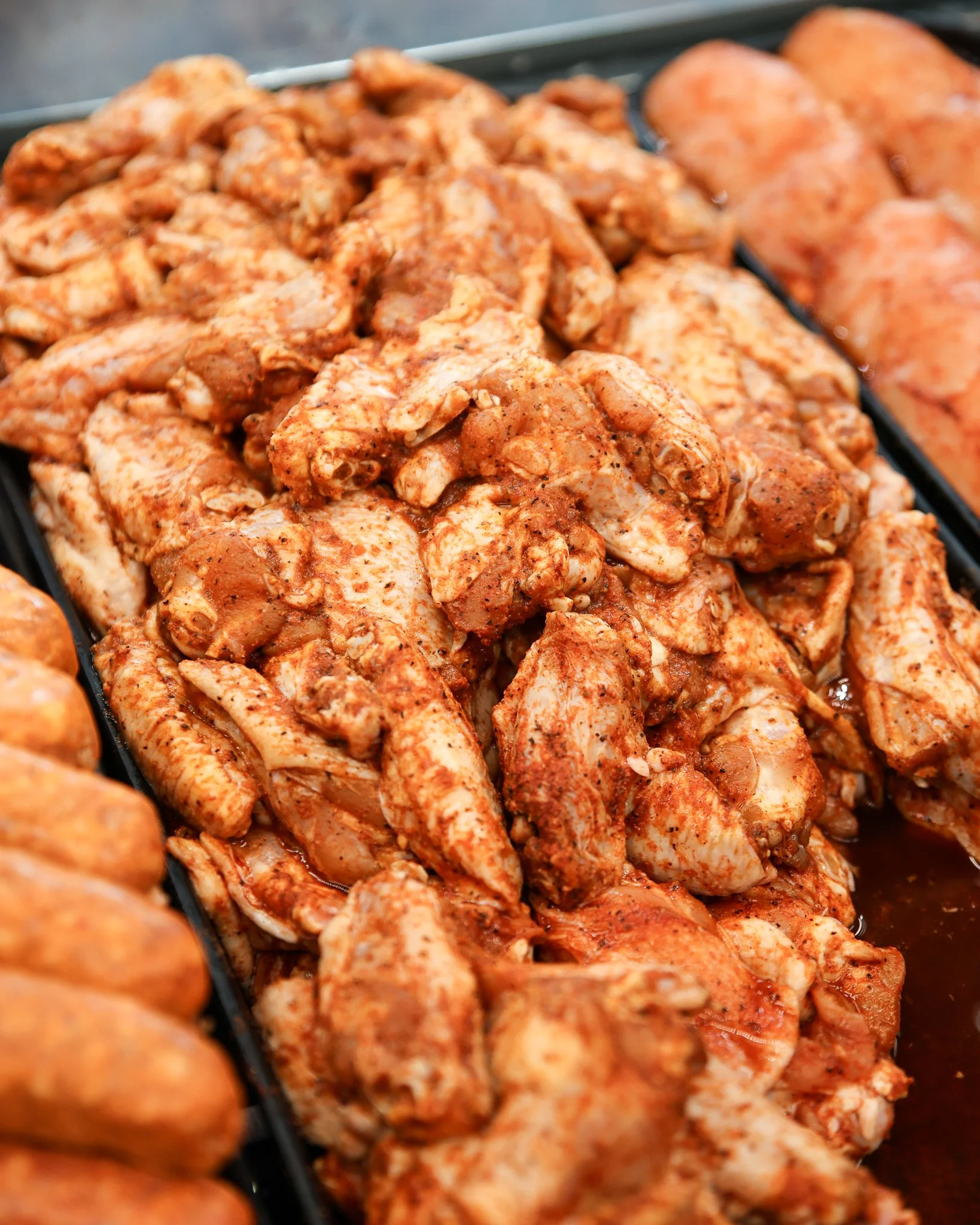 Raw seasoned chunks of chicken meat in a black tray.
