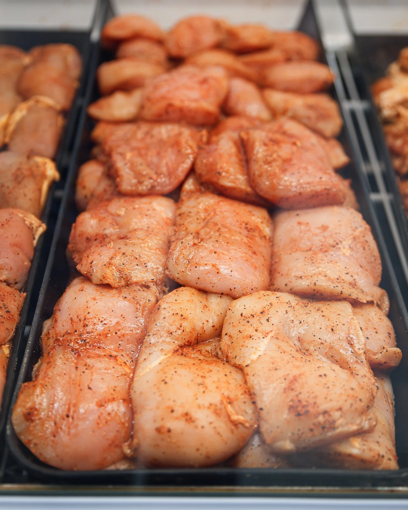 Raw seasoned chicken pieces arranged on a black tray.