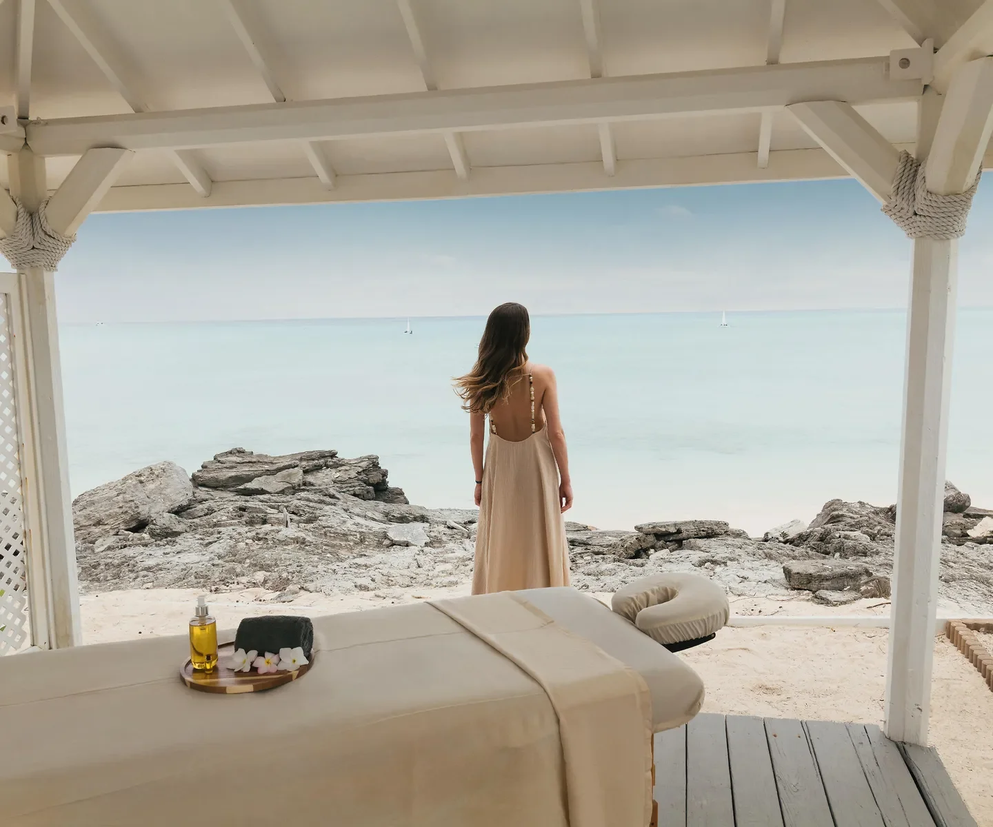 A woman in a pink swimsuit swimming in clear turquoise water near a green tropical shoreline with palm trees.