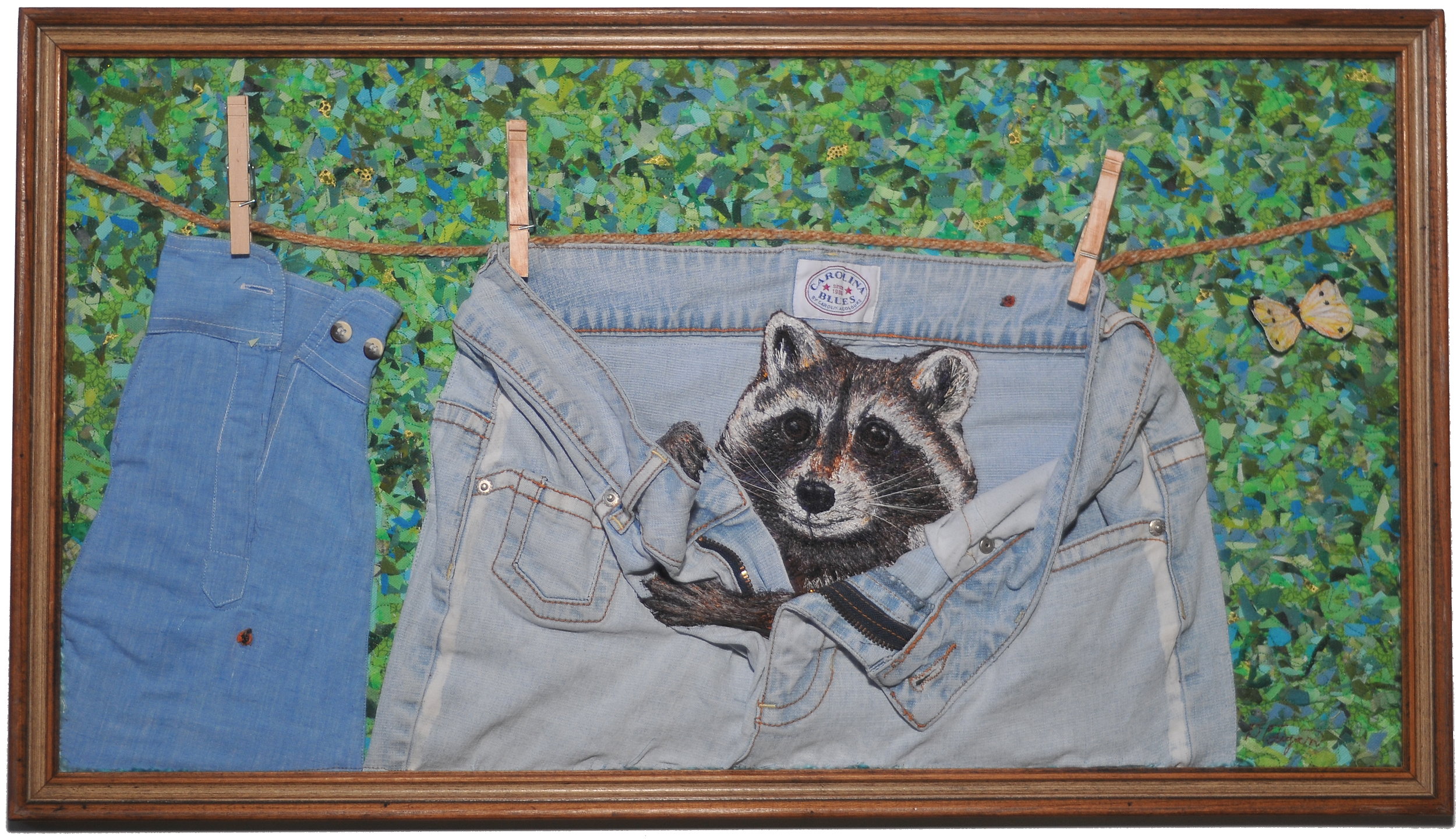 Mixed media artwork of denim jeans and a quilteraccoon, with a background of green foliage and a butterfly, framed in wood.