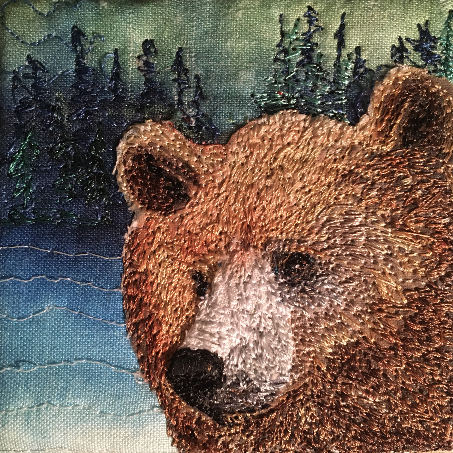 Quilt and thread painting of a bear's face with a forest background.