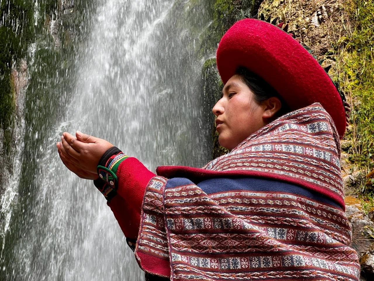 Person in traditional attire holding hands out near waterfall