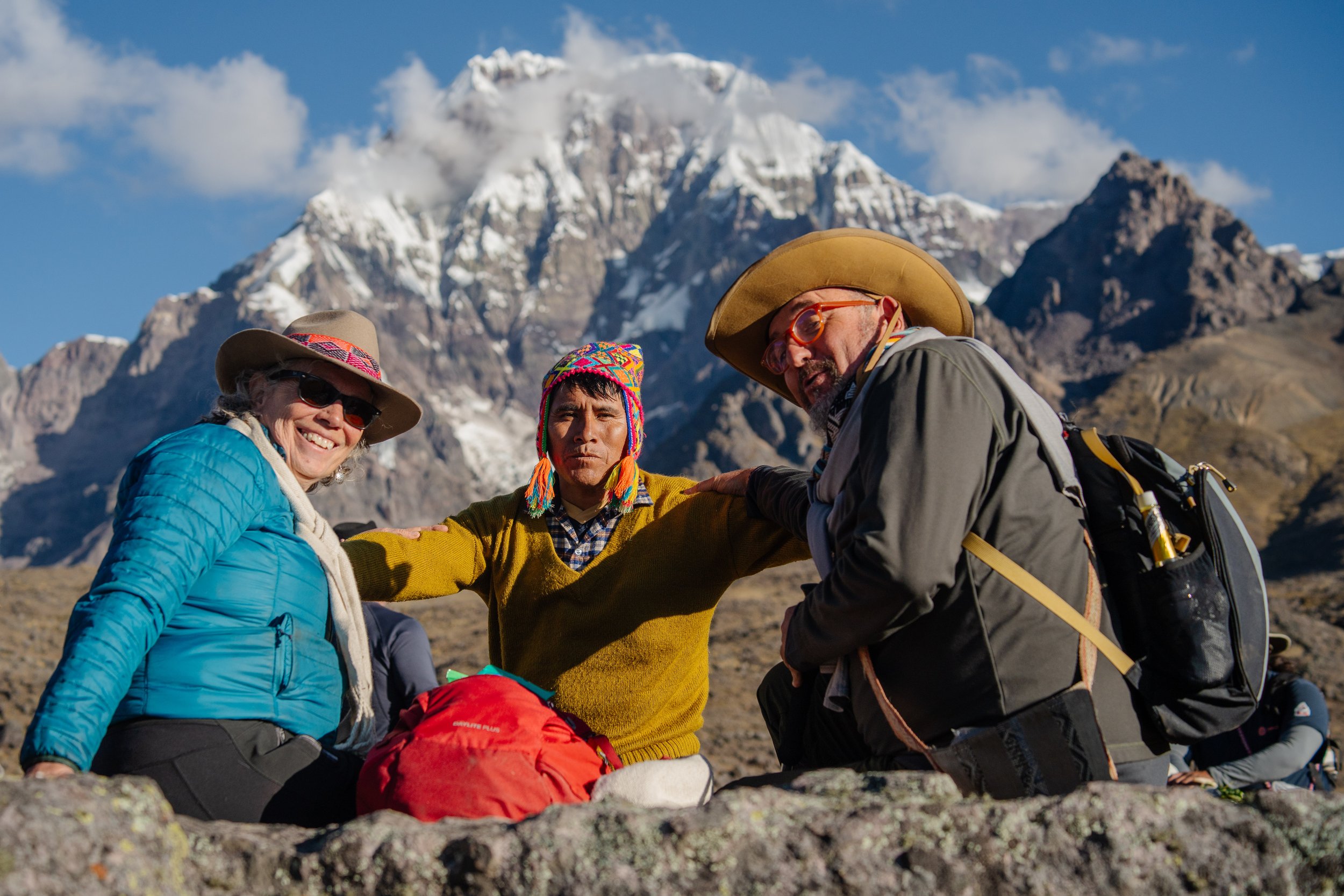 Three people sitting on rocks with a snowy mountain in the background.
