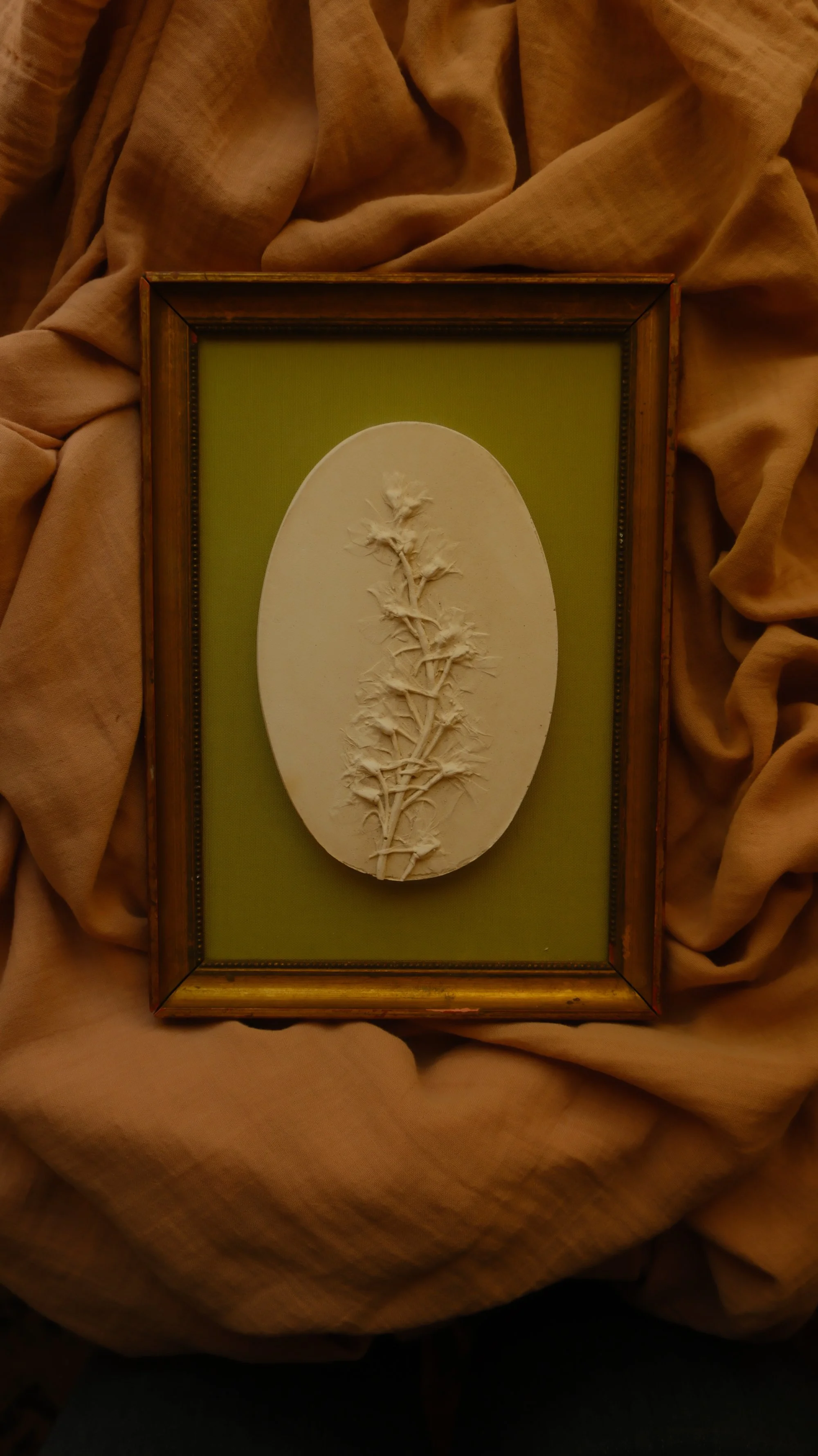 Oval plaster bas-relief of a single larkspur stem mounted in a vintage gilt frame with olive-green fabric.